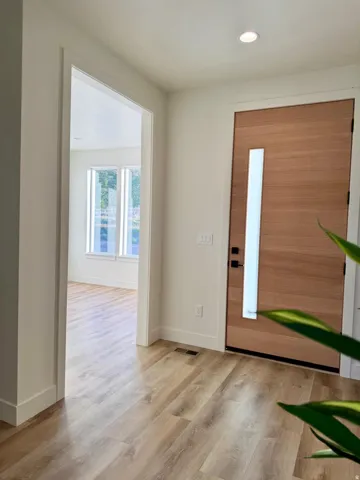 Entryway featuring contemporary wood-paneled door with vertical frosted glass insert, wood-finish flooring, and recessed ceiling lighting