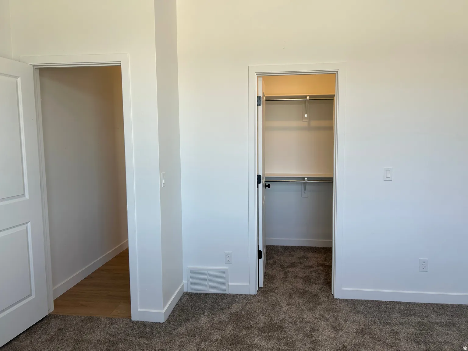 Plush carpeted flooring and white painted walls characterize this interior space, featuring a closet with integrated shelving and hanging rods