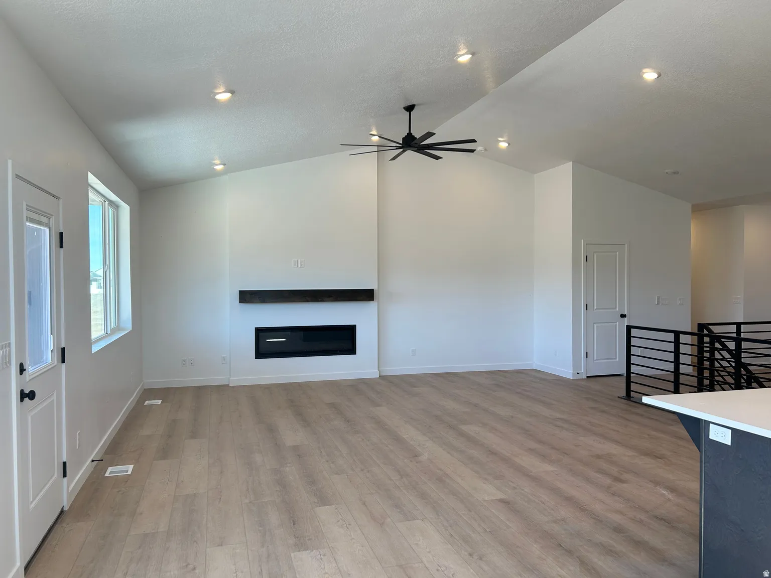 Spacious living area featuring a vaulted ceiling with recessed lighting, a modern linear electric fireplace with a wood mantel, wood-finish flooring, and a contemporary ceiling fan