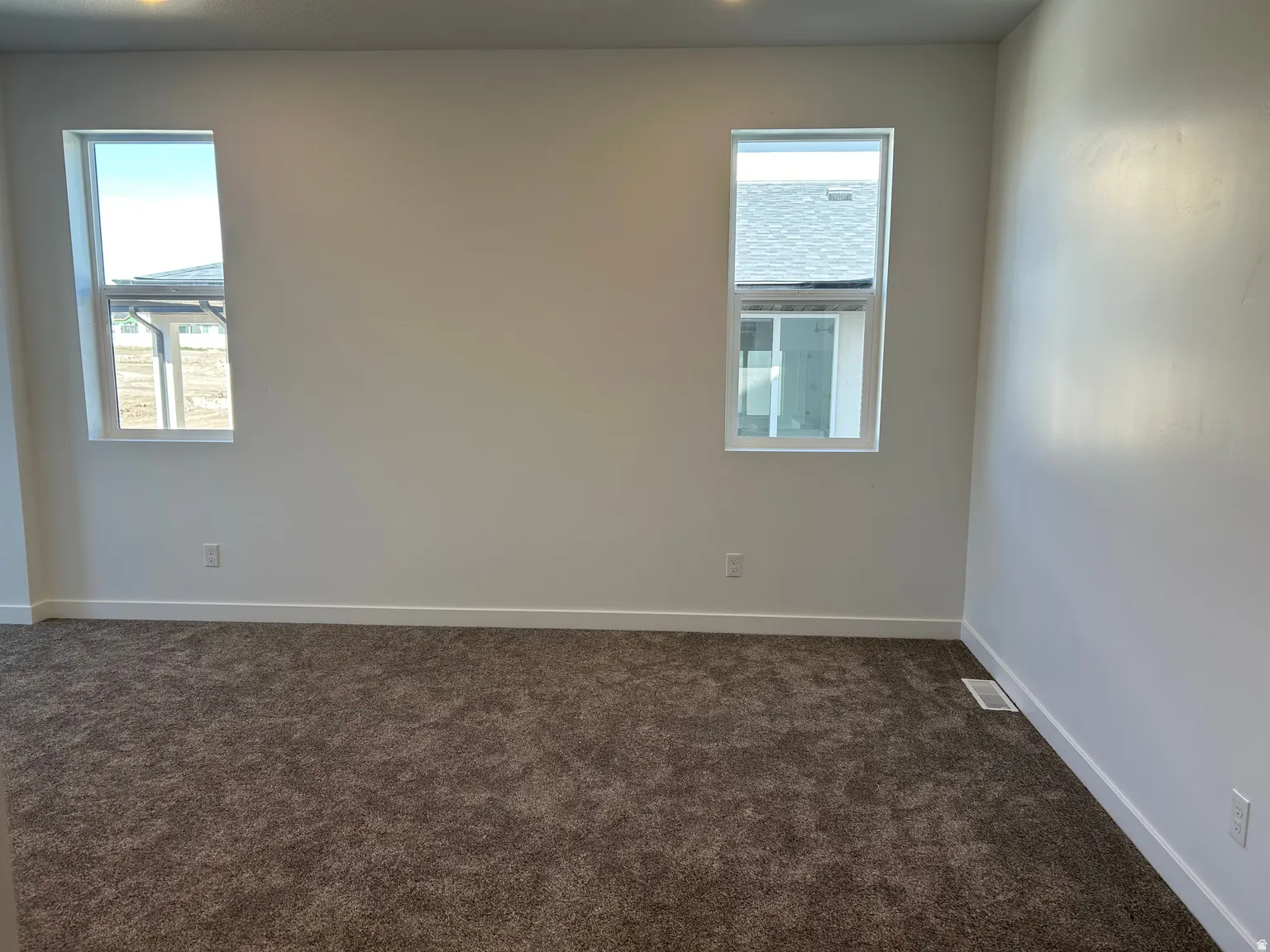 Spacious room featuring neutral wall paint, two white-framed windows, recessed lighting, plush carpet flooring, and white baseboards