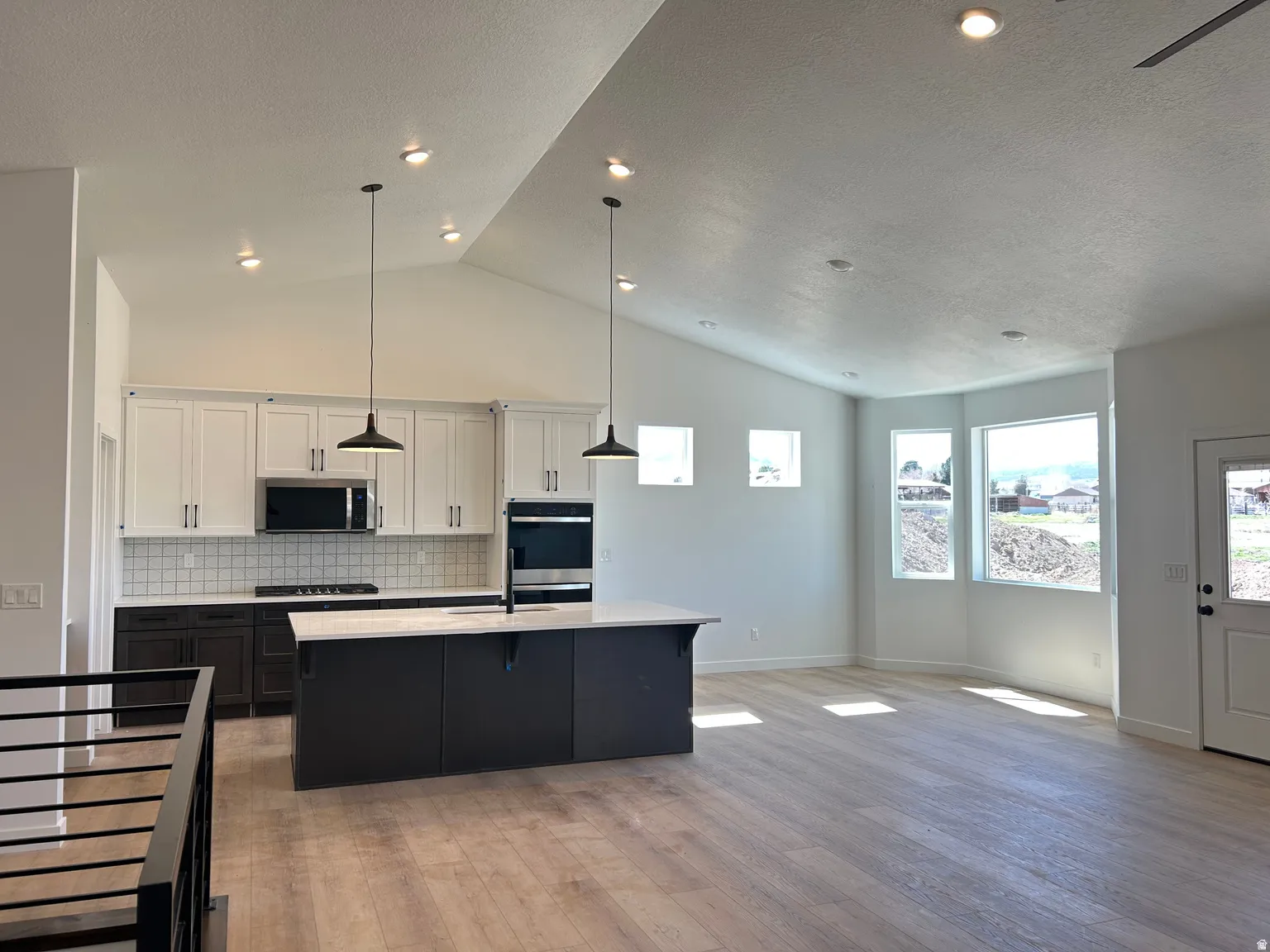 Open-concept living space featuring vaulted ceilings with recessed lighting, light wood-finish flooring, and a contemporary kitchen