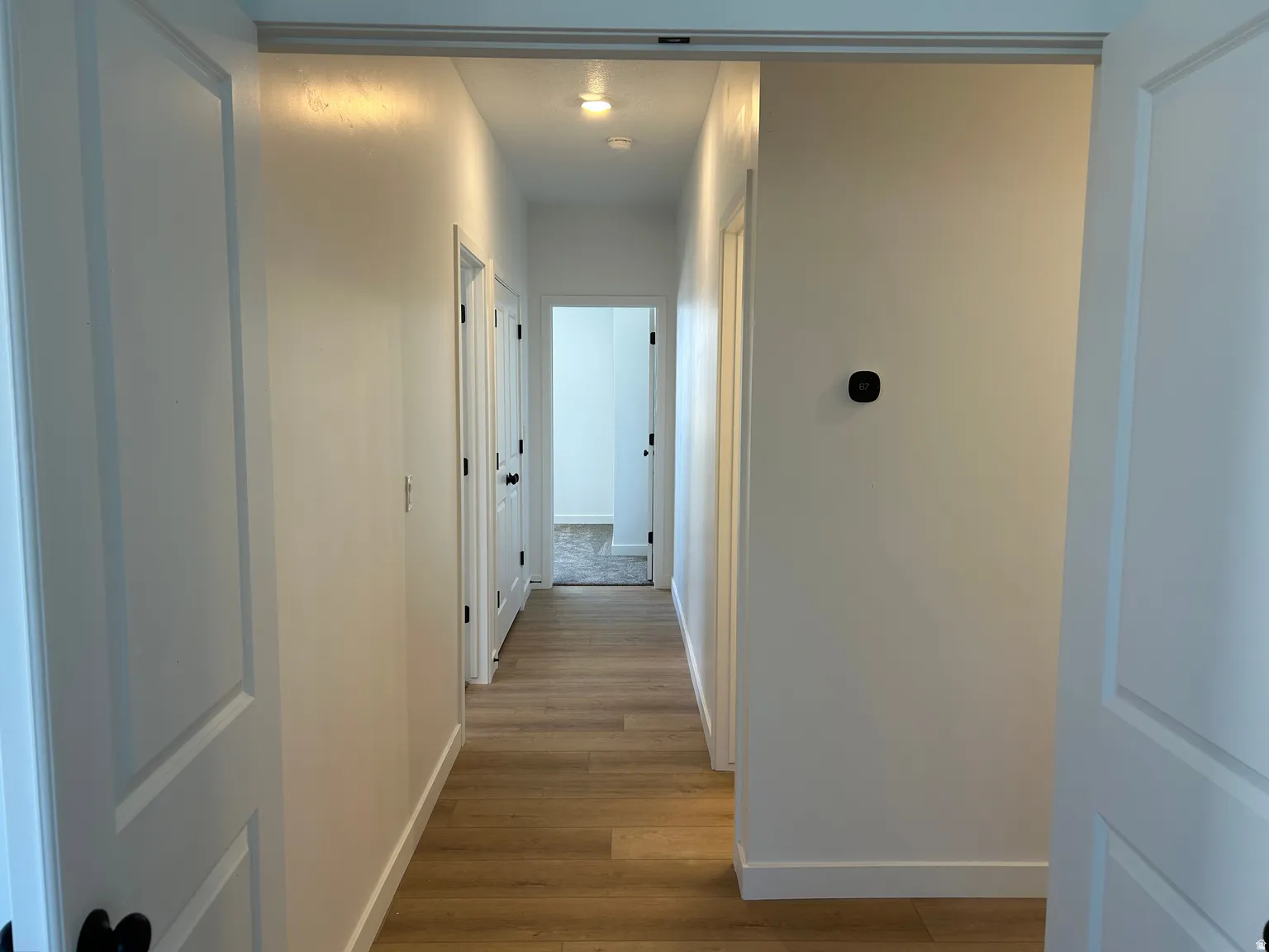 Hallway with wood-finish flooring, white walls, and recessed lighting