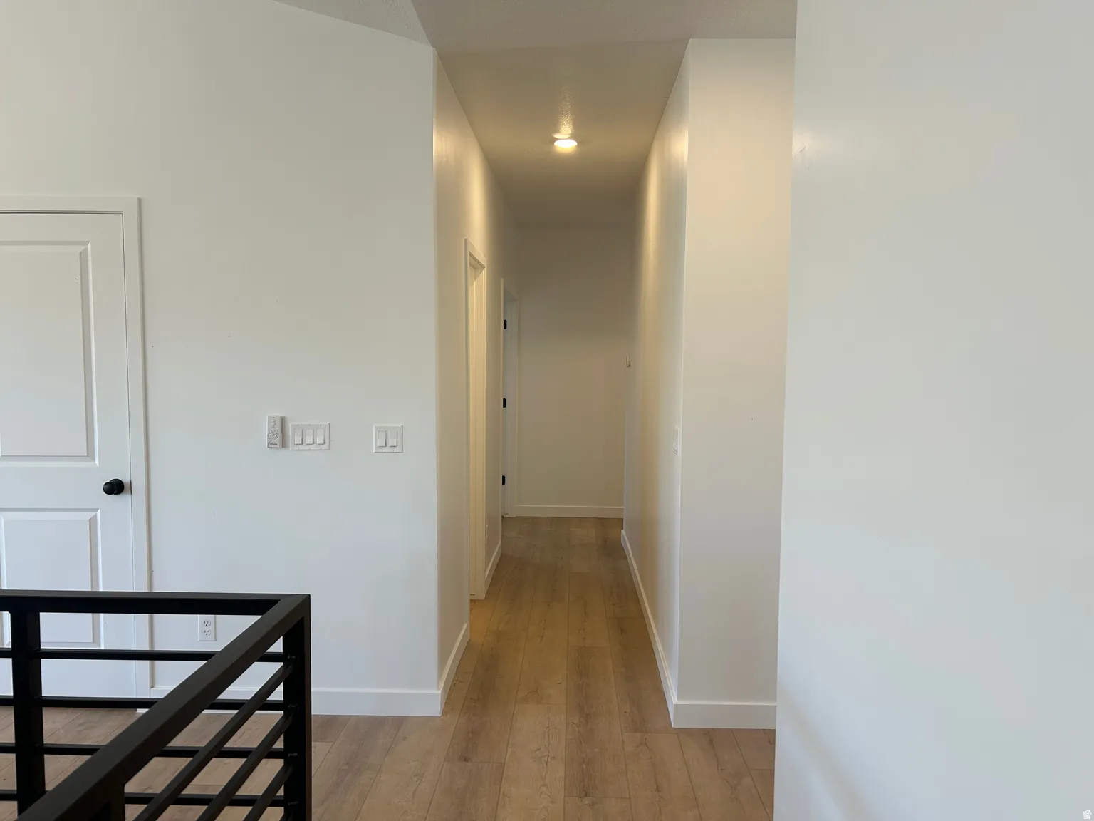 Hallway with wood-finish flooring, white baseboards, and a contemporary black metal railing