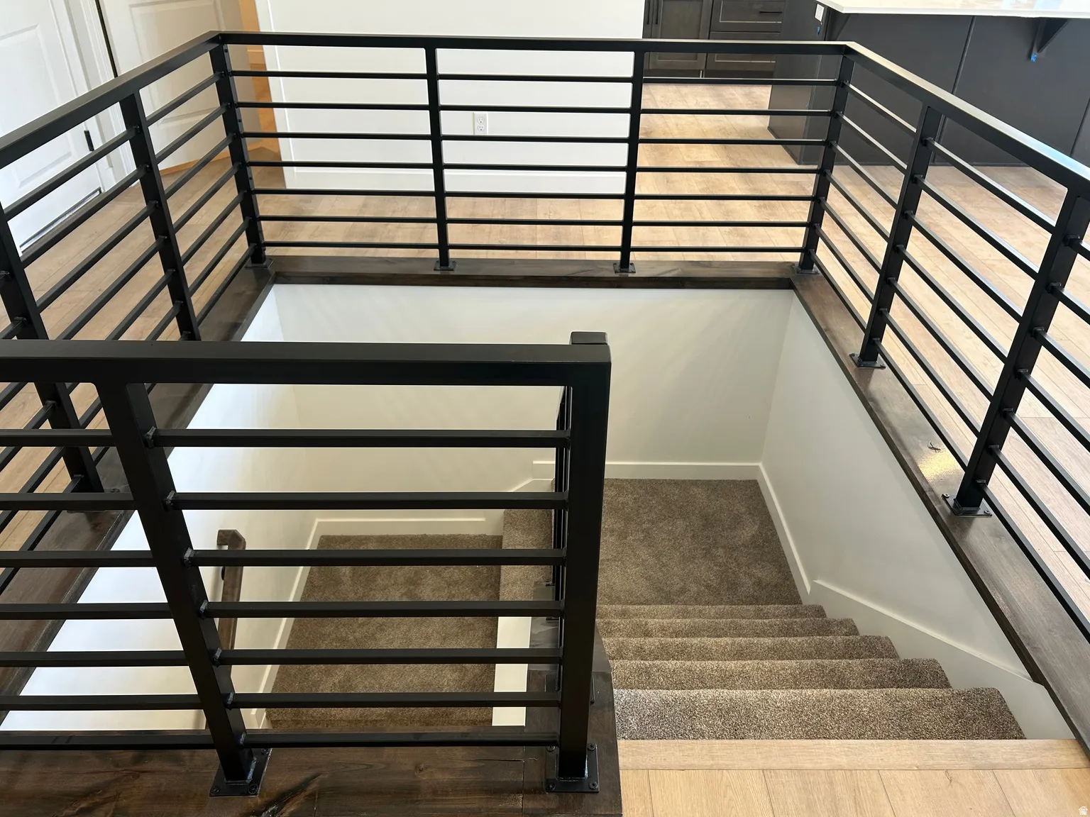 Modern stairwell featuring a black metal railing with horizontal bars, dark wood-finish newel posts, and a carpeted descent