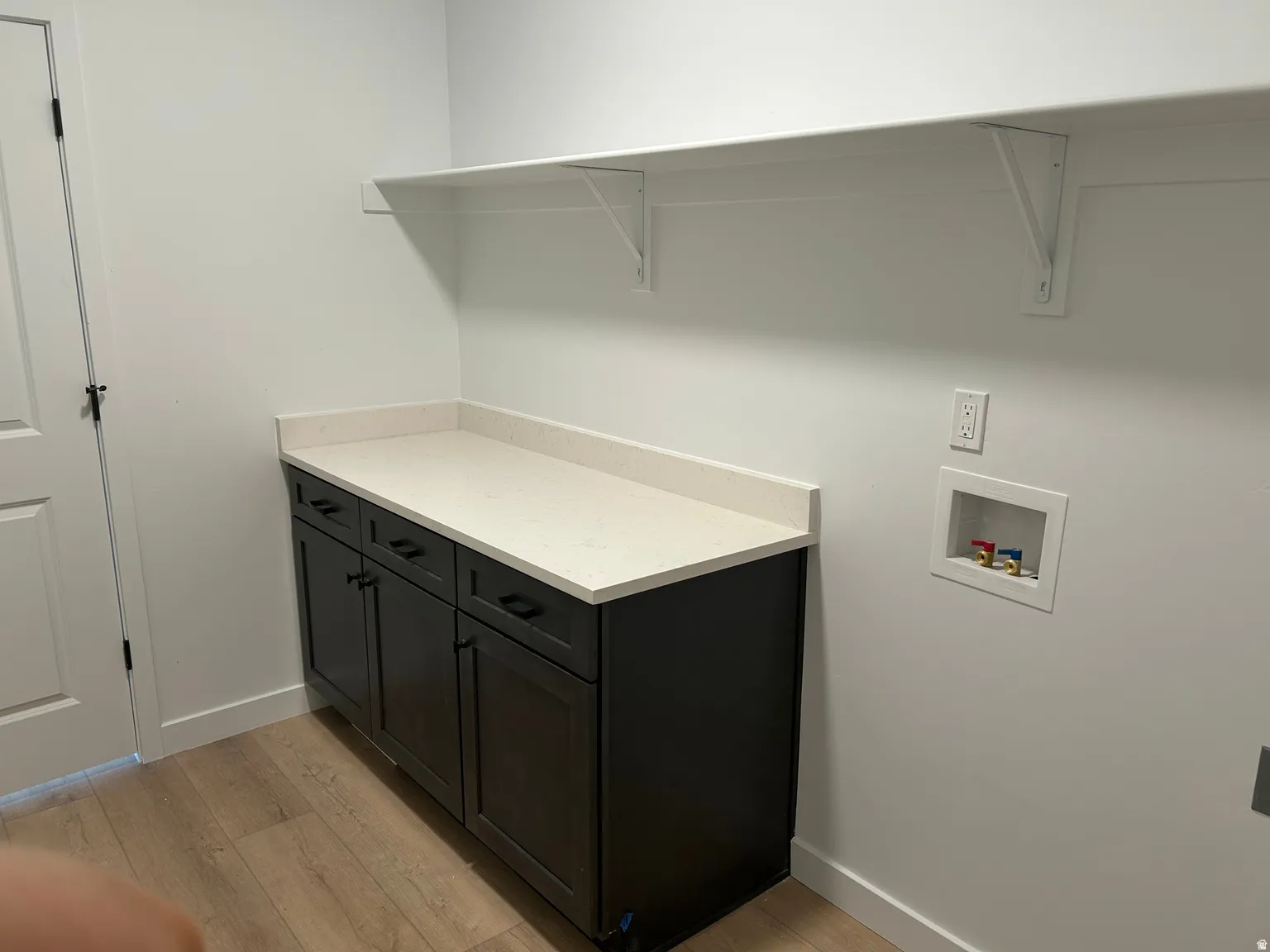 Laundry area featuring dark wood-finish cabinetry, a light-toned countertop, and light wood-finish flooring