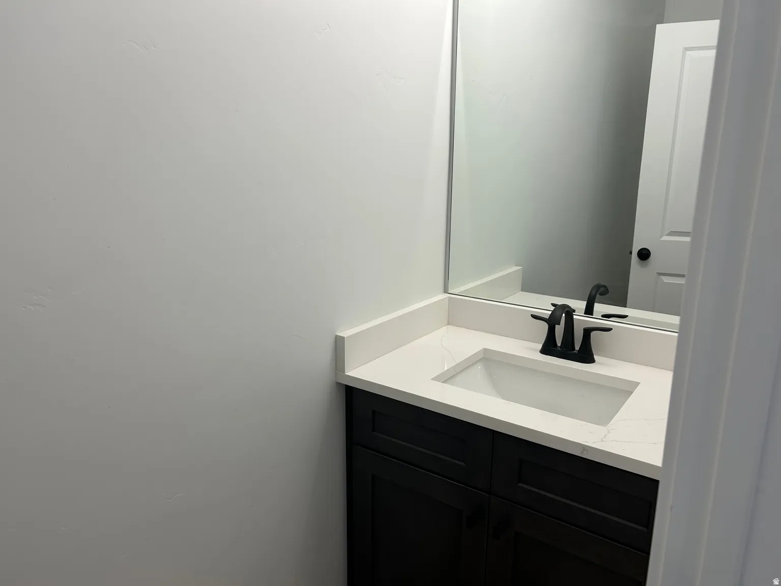 Bathroom featuring a dark wood-finish vanity with a white countertop, integrated sink, and matte black faucet