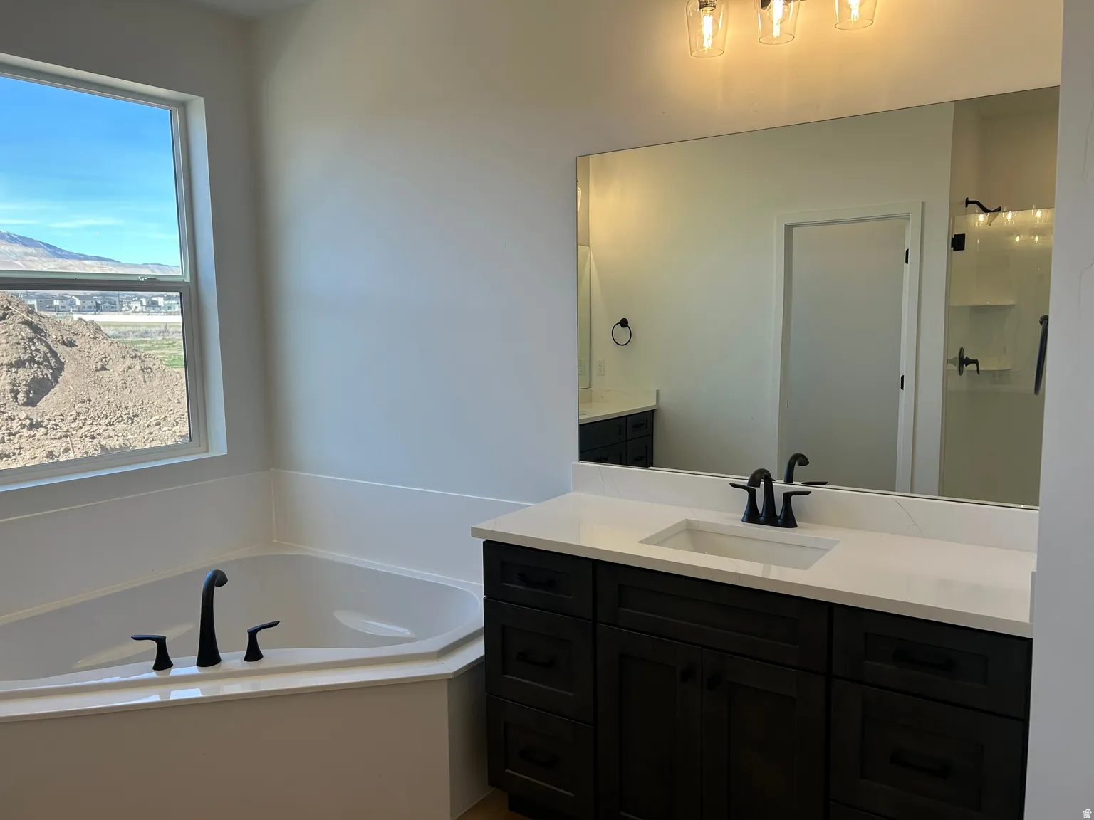 Bathroom featuring a built-in corner soaking tub with matte black fixtures, a single vanity with dark wood-finish cabinetry, a white countertop, and an integrated rectangular sink