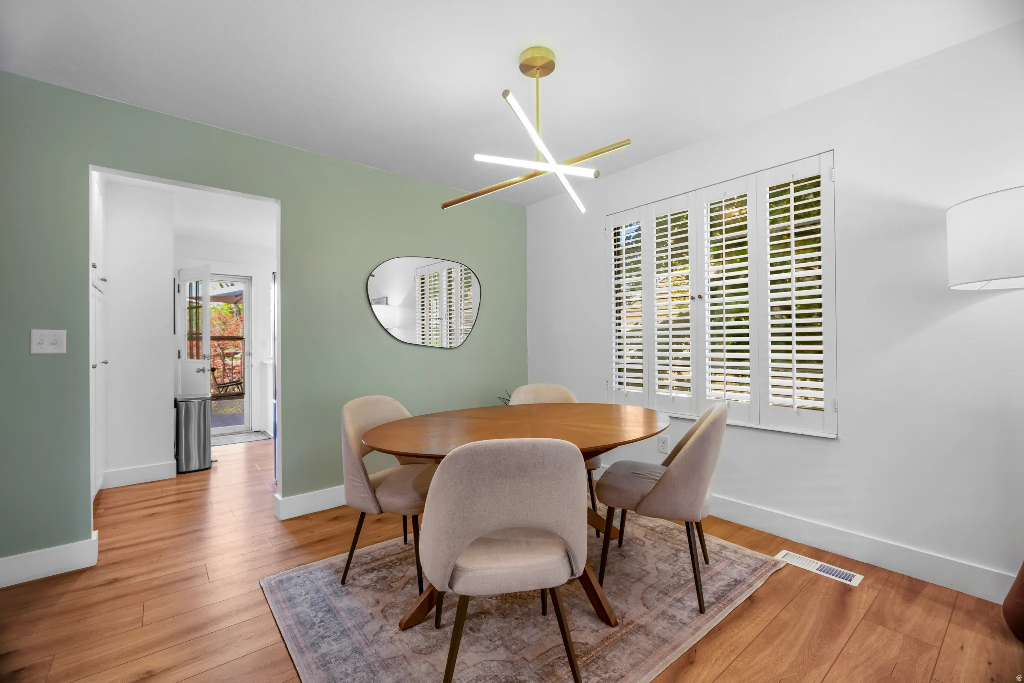Dining space featuring wood-finish flooring, a contemporary chandelier, white window shutters, and a contrasting accent wall
