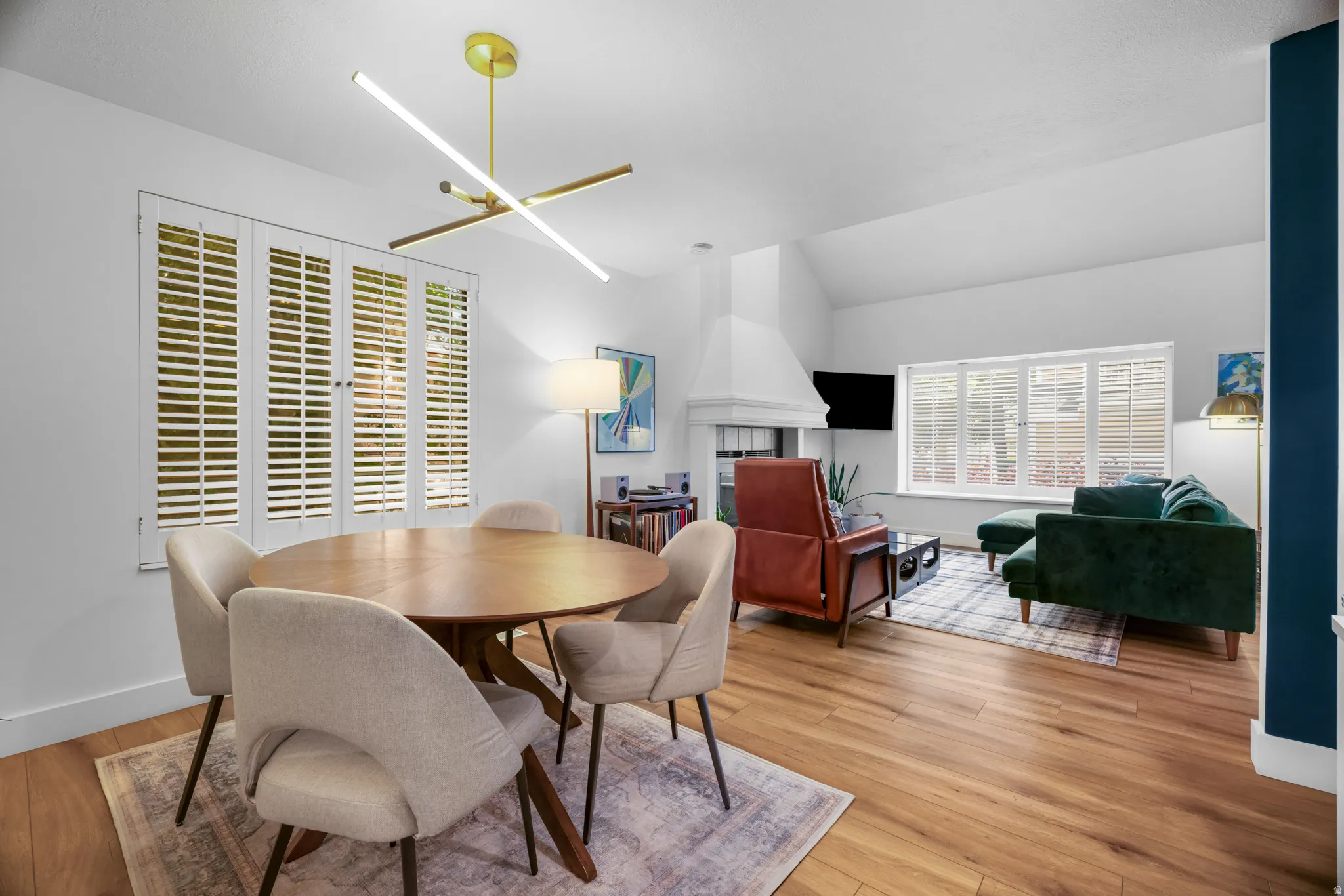 Open concept living and dining area featuring wood-finish flooring, vaulted ceilings, and white plantation shutters on multiple windows