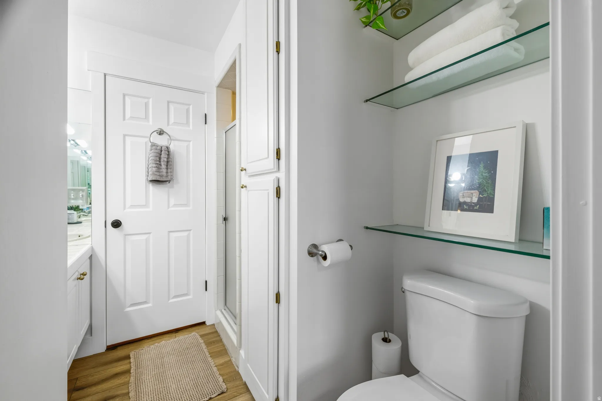 Bathroom featuring glass shelving, white cabinetry, wood-finish flooring, a paneled door, and a shower enclosure
