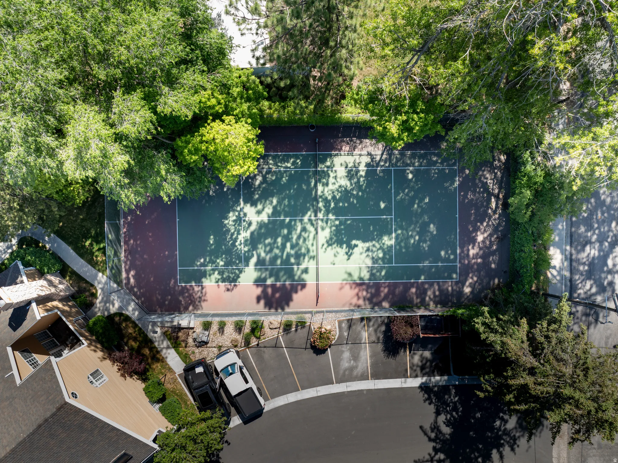 Full-size tennis court with green and red playing surfaces, surrounded by mature trees