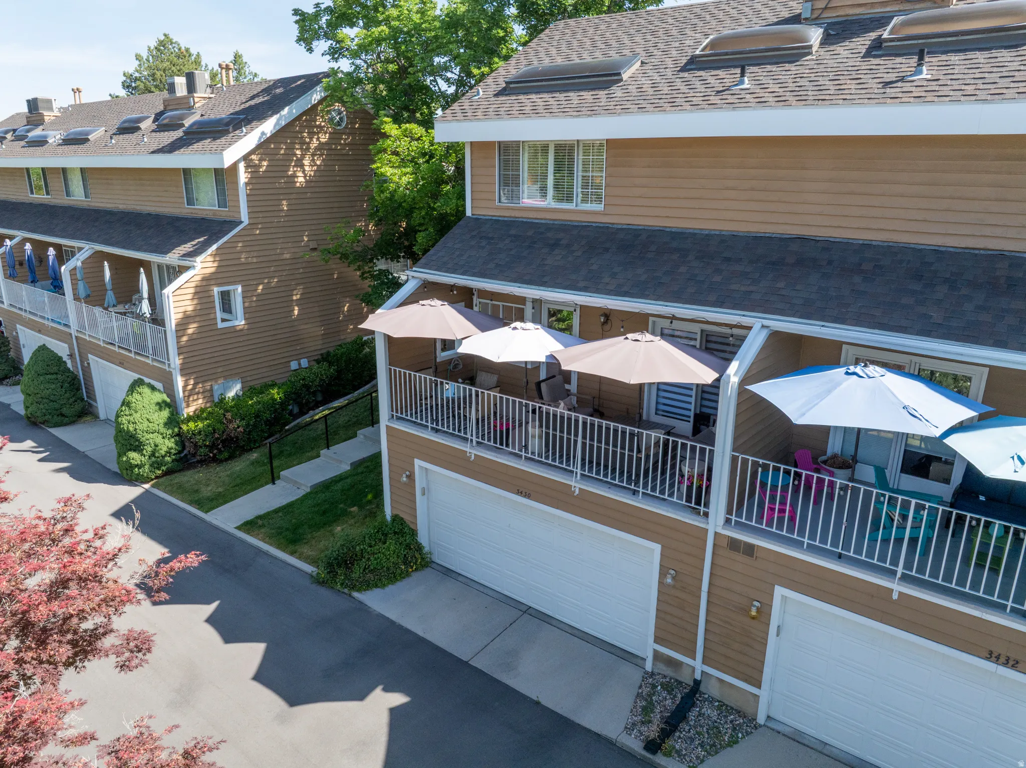 Townhome exterior featuring tan siding, white garage doors, and dark shingle roofing