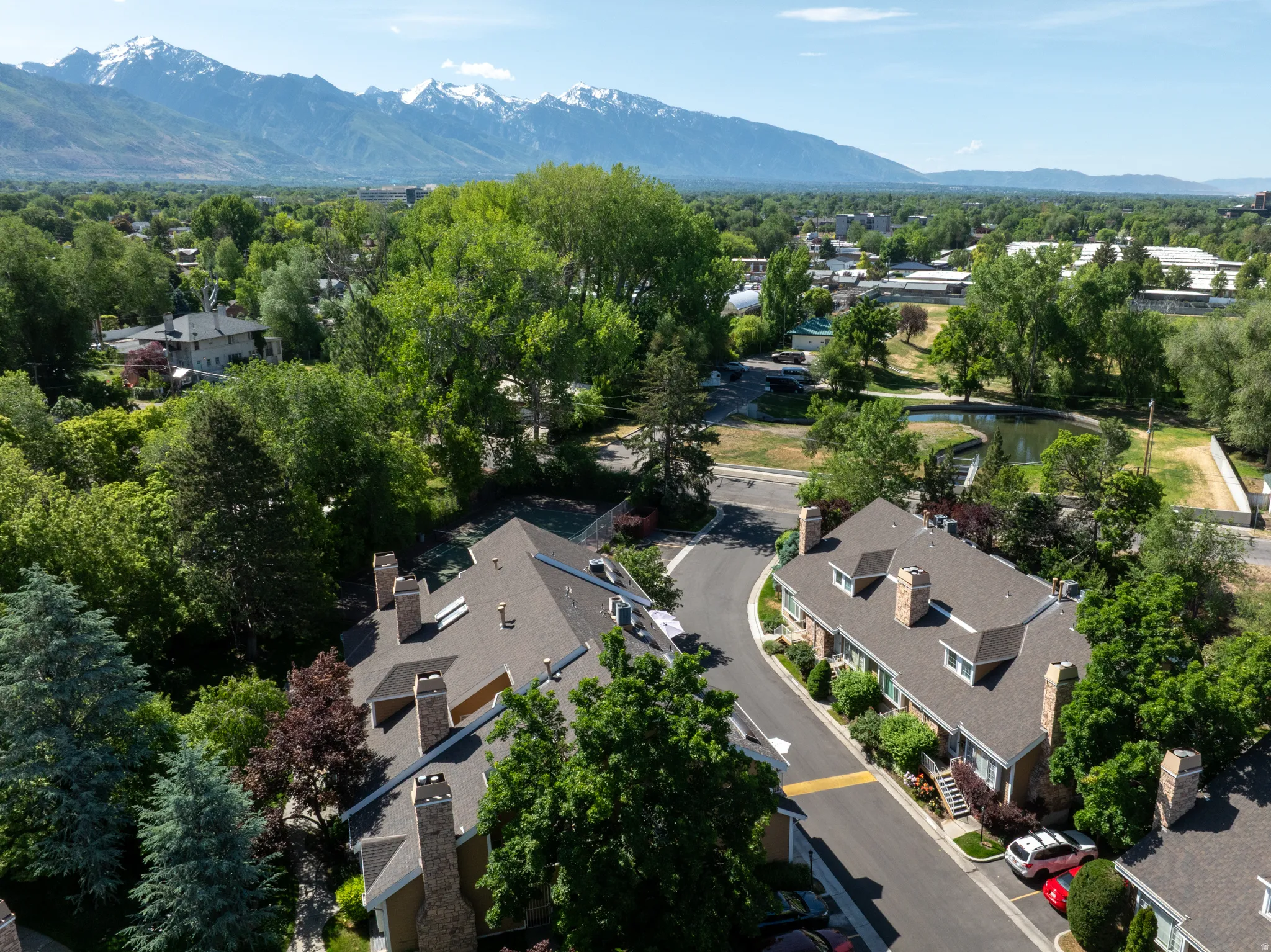 Townhome community with pitched roofs, multiple chimneys, and dormer windows, surrounded by mature trees and landscaping