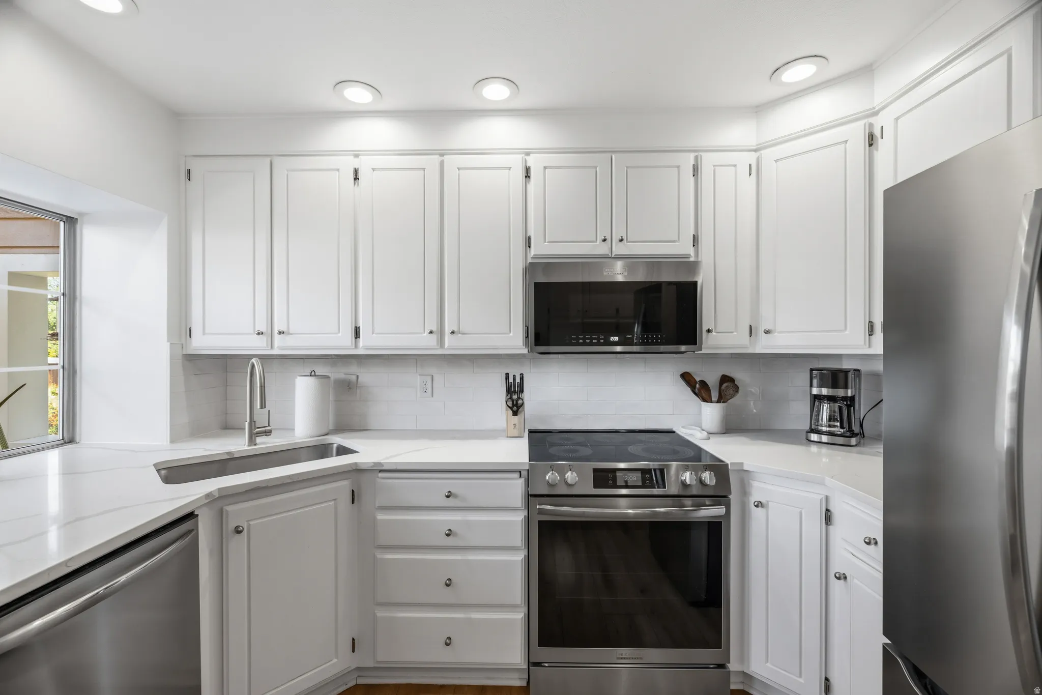 White cabinetry with stainless steel appliances, including an electric range, microwave, and dishwasher