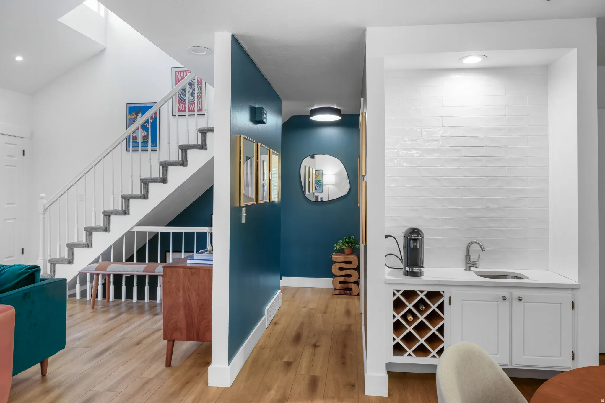 Built-in wet bar with white cabinetry, wood-finish flooring, staircase with white balusters, and a skylight