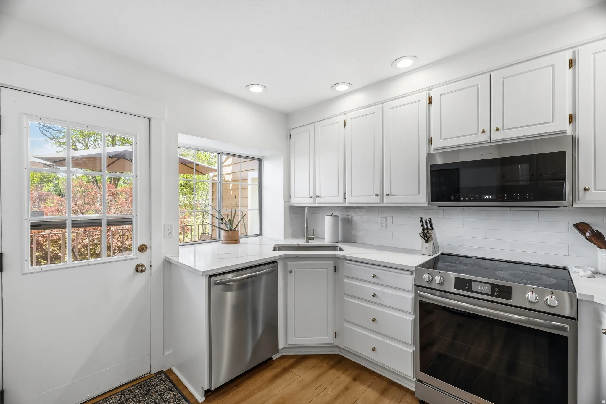 Kitchen featuring white cabinetry, stainless steel appliances, white subway tile backsplash, white countertops, and wood-finish flooring