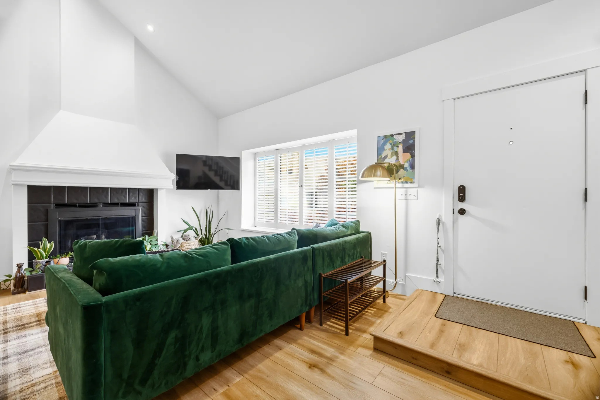 Living area featuring wood-finish flooring, a fireplace with a black tile surround, and a vaulted ceiling