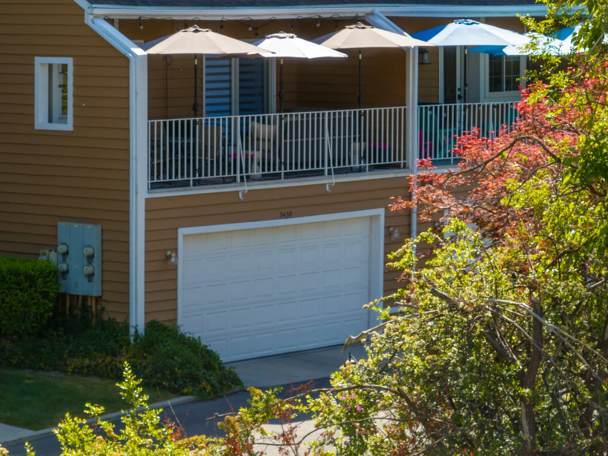 Two-story residential structure featuring a white garage door, an upper-level balcony with white railings, and a horizontal siding facade
