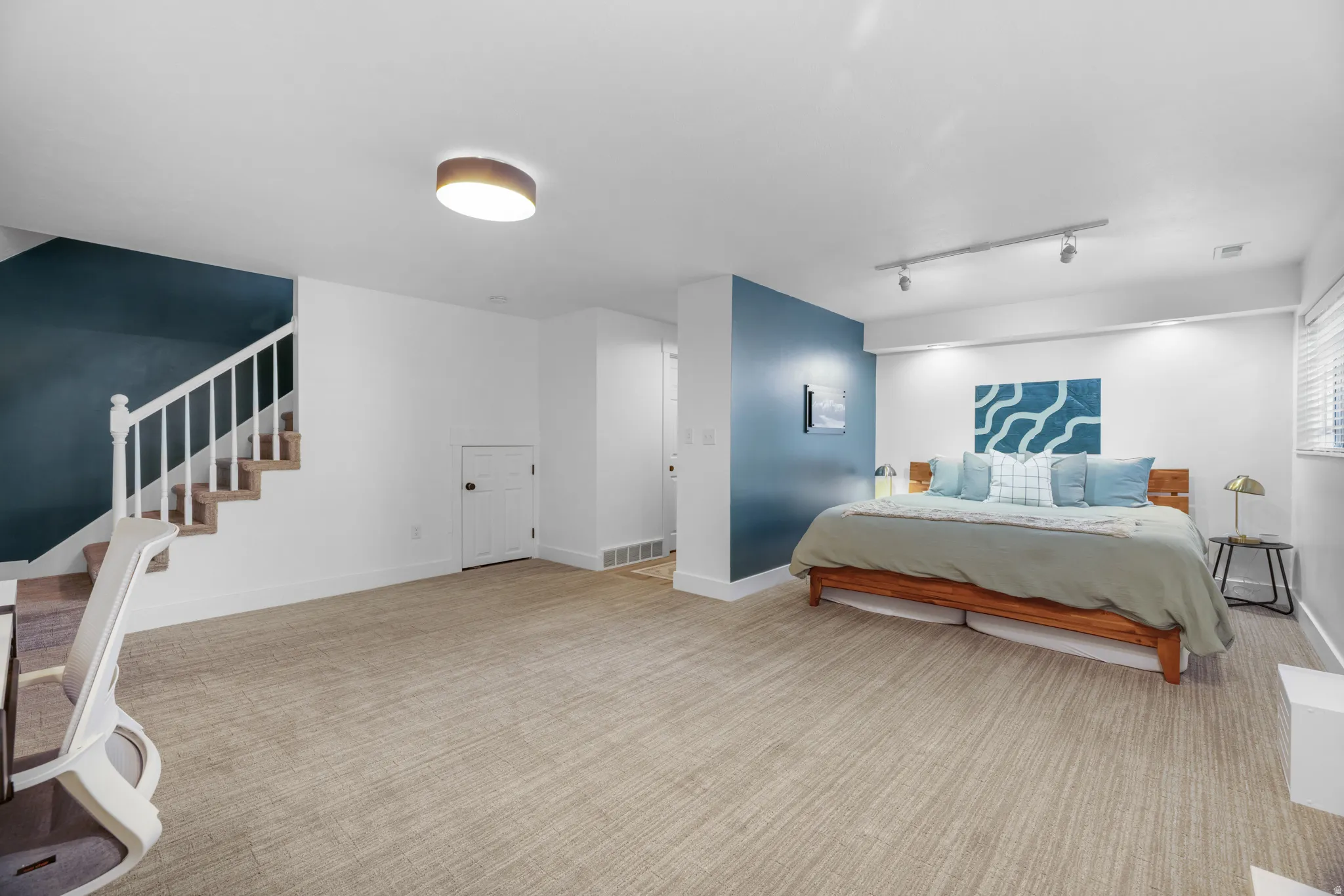 Spacious room with plush carpeting, a built-in staircase with white balusters, and a recessed storage door