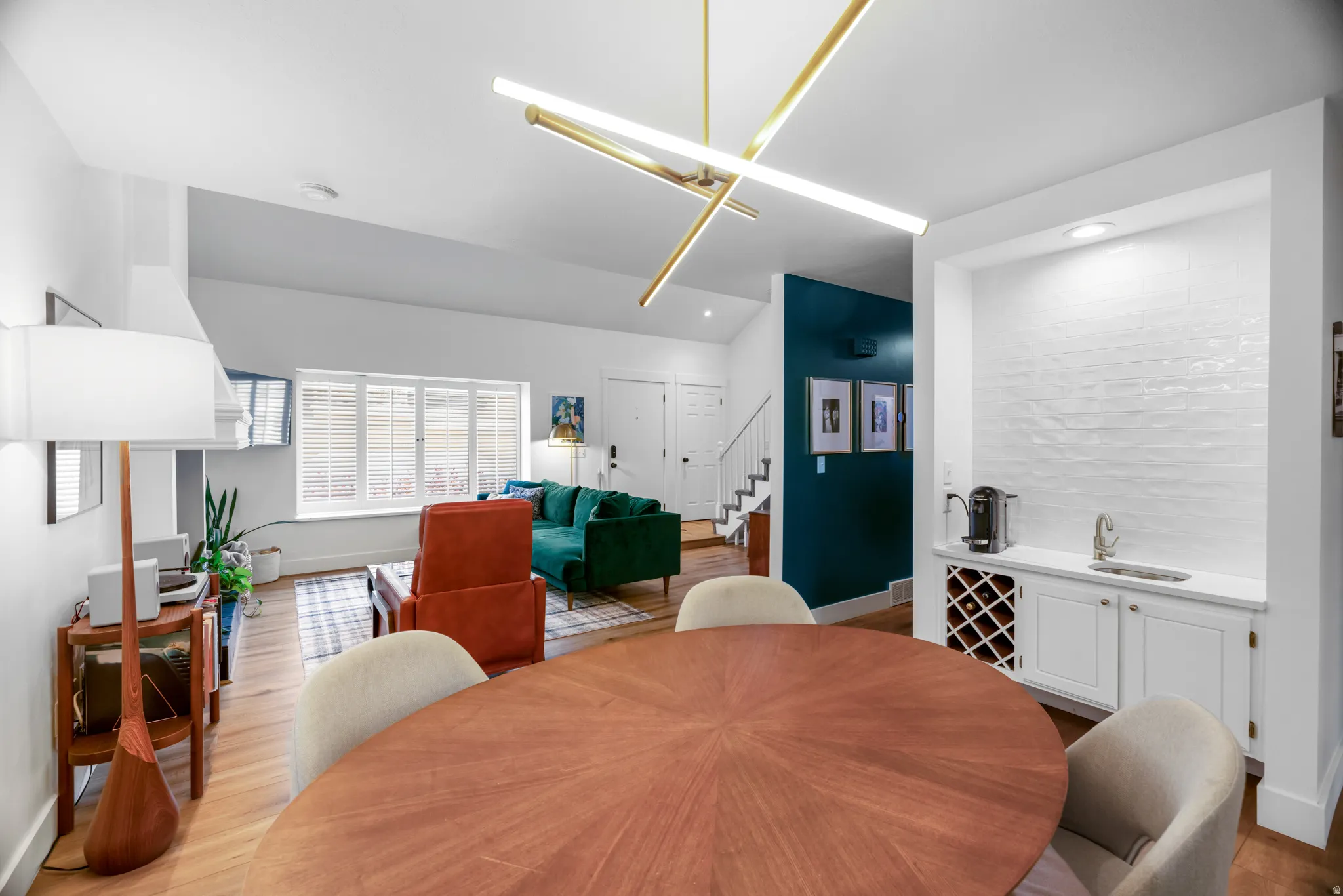 Open-concept living area featuring a prominent linear chandelier, wood-finish flooring, and a built-in wet bar with a wine rack