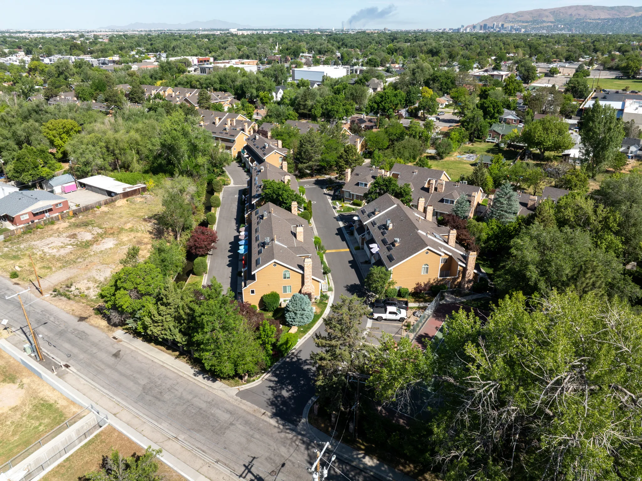 Aerial perspective showcasing a residential community with numerous brown-roofed townhomes and ample mature trees