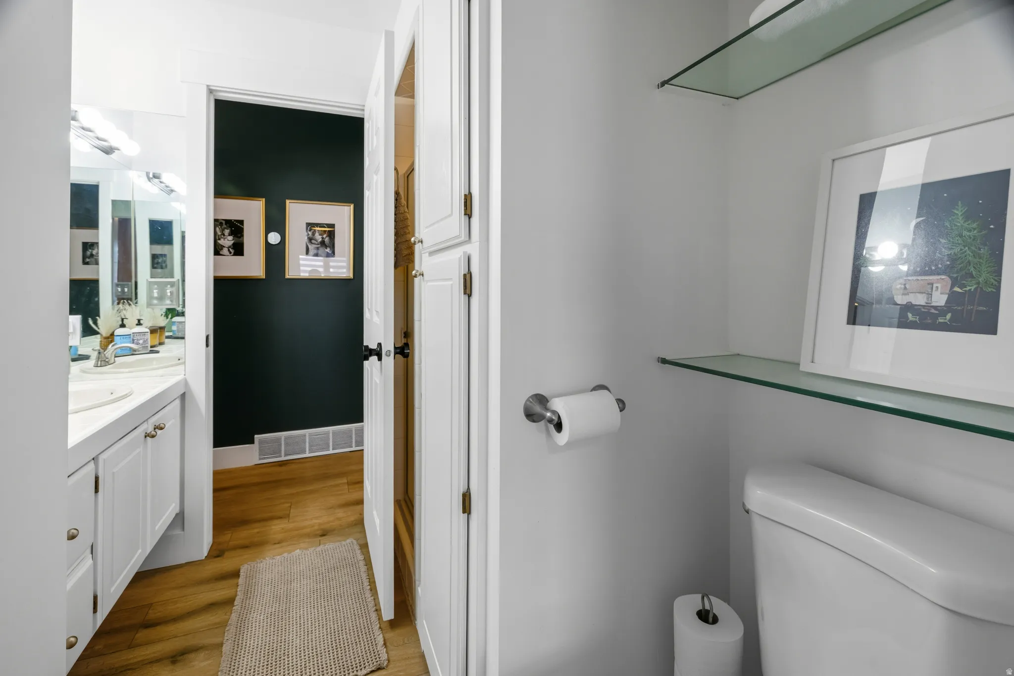 Bathroom featuring a white toilet, glass shelving, and a vanity with dual sinks