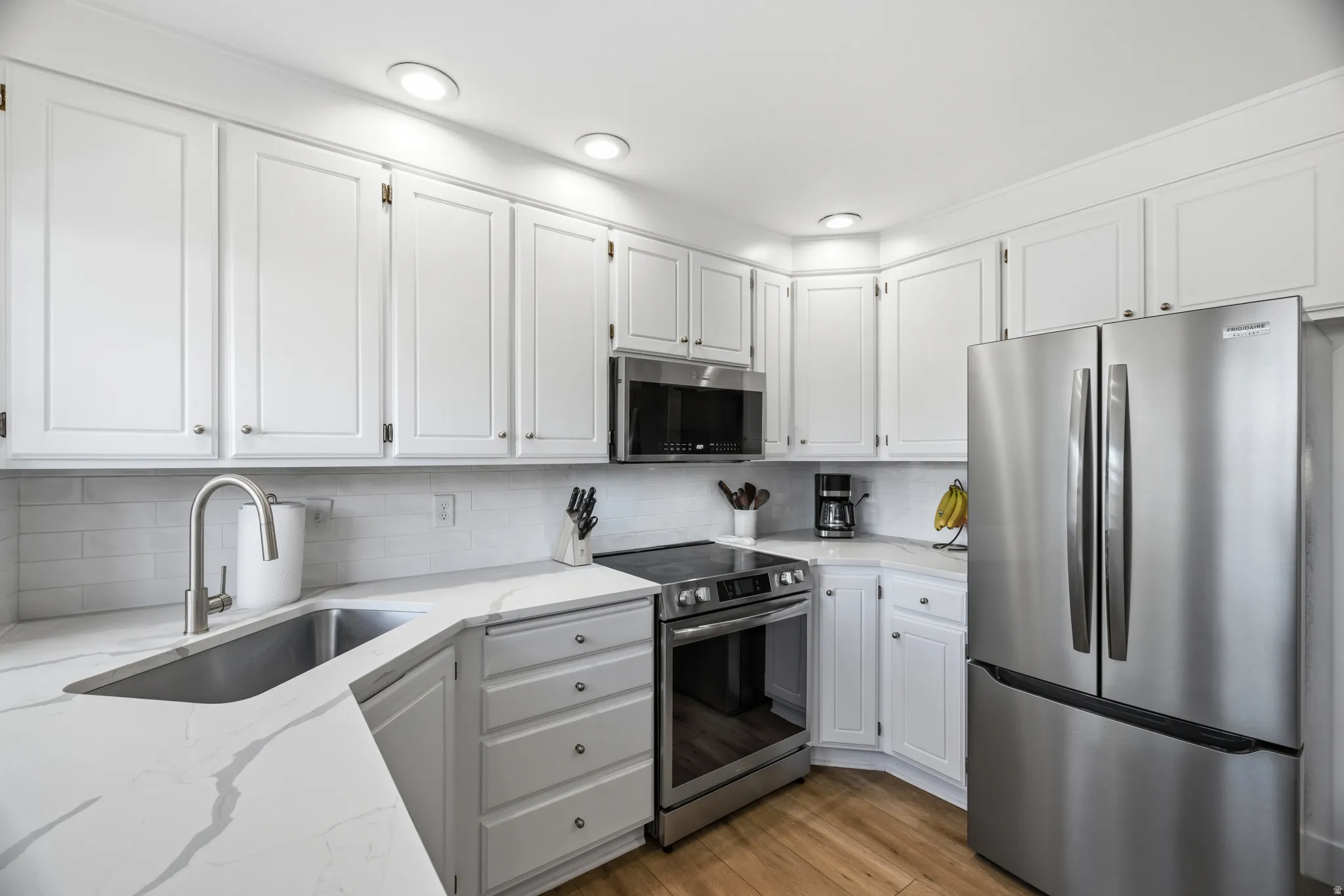 Updated kitchen featuring white shaker-style cabinetry, recessed lighting, and wood-finish flooring