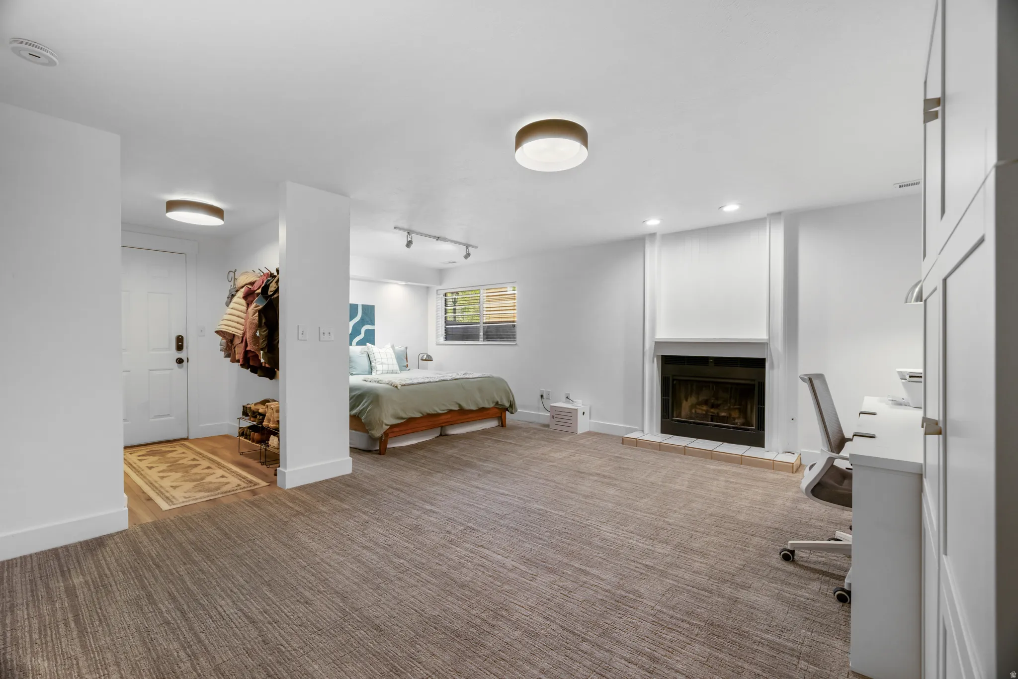 Spacious room with textured carpet flooring, featuring a fireplace with a white mantel and tile hearth, along with built-in white cabinetry