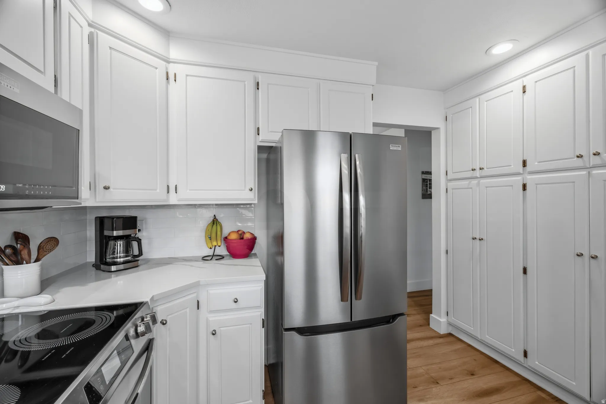 Kitchen featuring extensive white cabinetry, stainless steel appliances, light countertops, a white subway tile backsplash, and wood-finish flooring