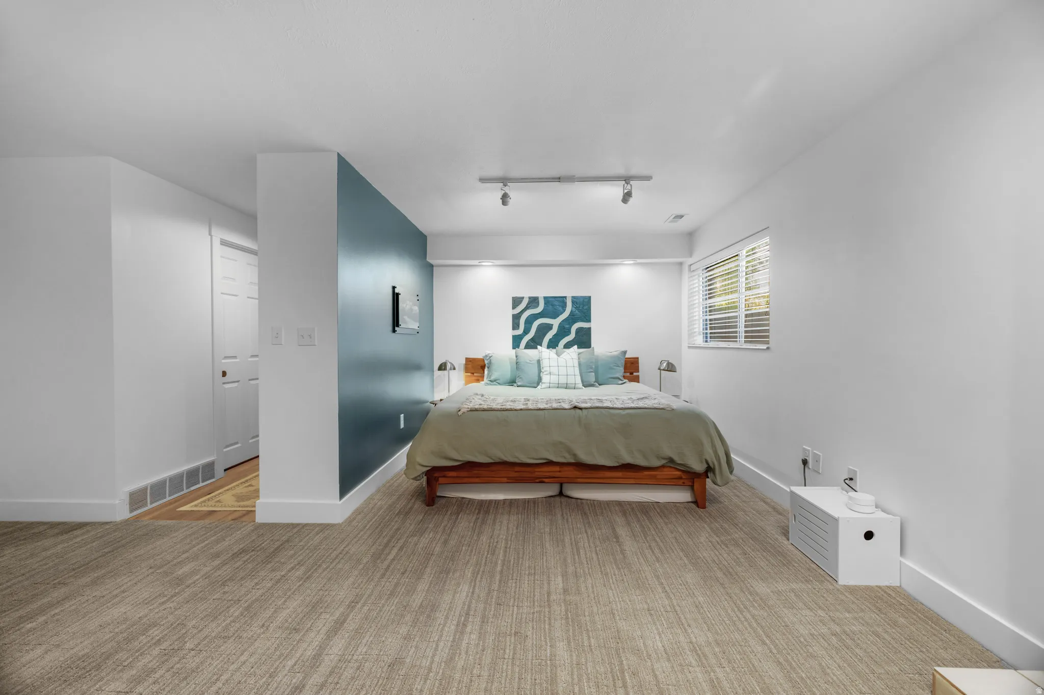 Spacious room featuring light-toned wood-finish flooring, a vibrant accent wall, recessed lighting, track lighting, and a window with blinds