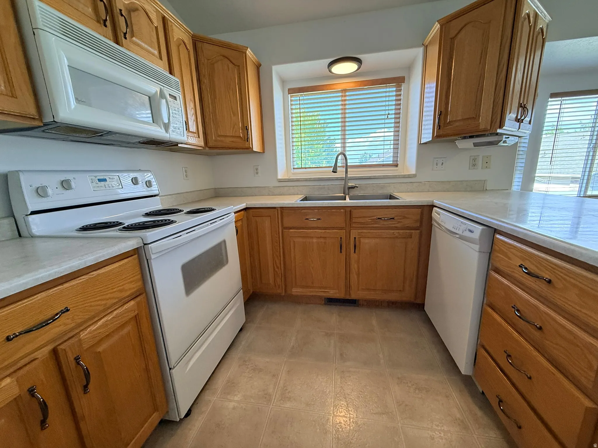 Kitchen featuring wood cabinetry, light-toned countertops, a stainless steel double basin sink, and an included electric range with an overhead microwave