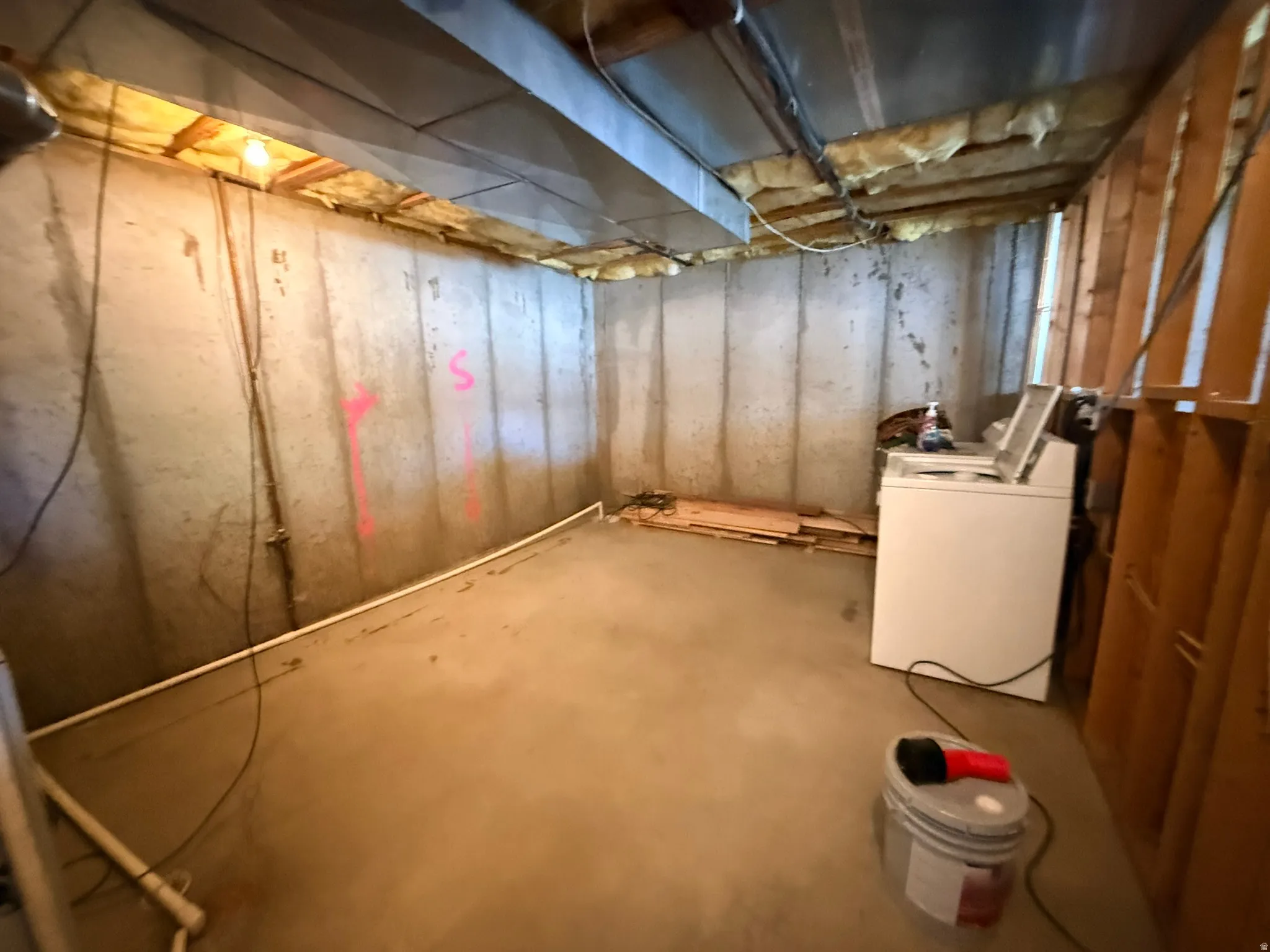 Unfinished basement space featuring exposed concrete walls and flooring, overhead ductwork, and visible wood framing