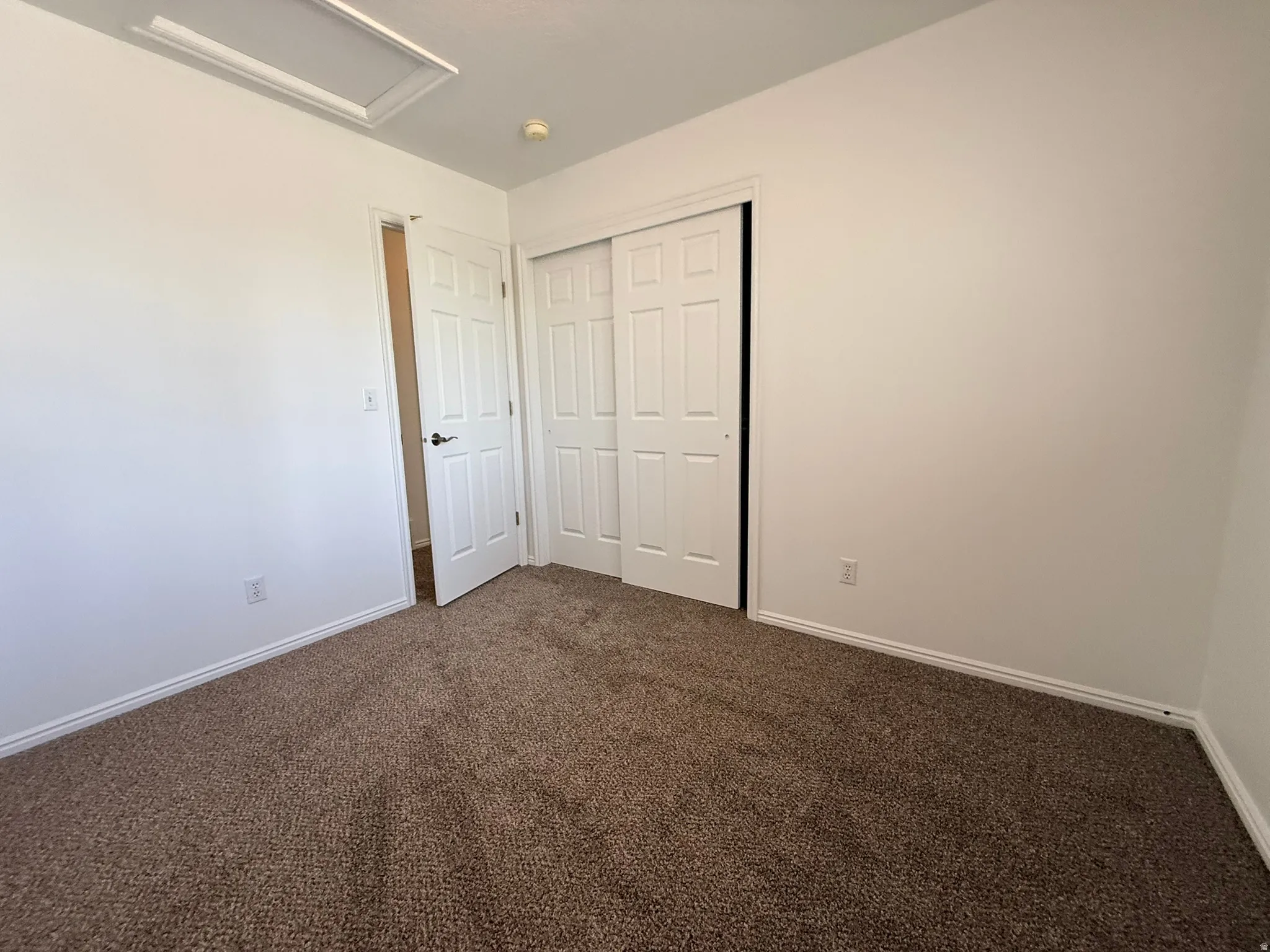Carpeted room featuring white walls, a white paneled door, and a white bi-fold closet