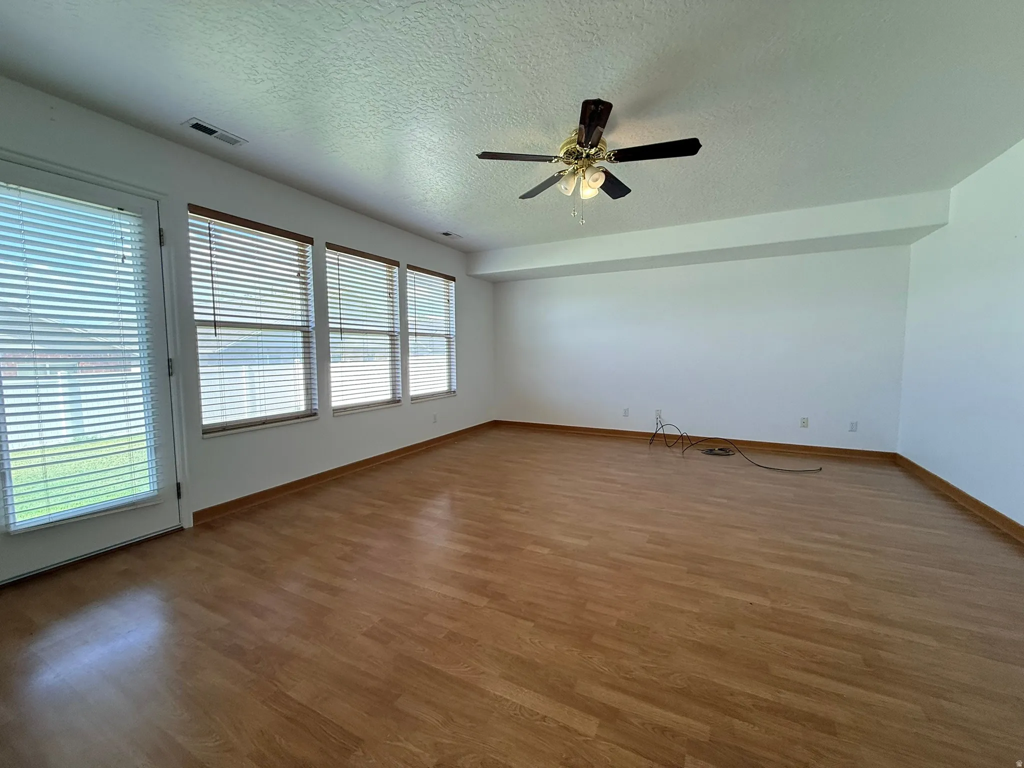 Spacious interior featuring wood-finish flooring, a ceiling fan with integrated lighting, multiple windows with blinds, and a white color palette
