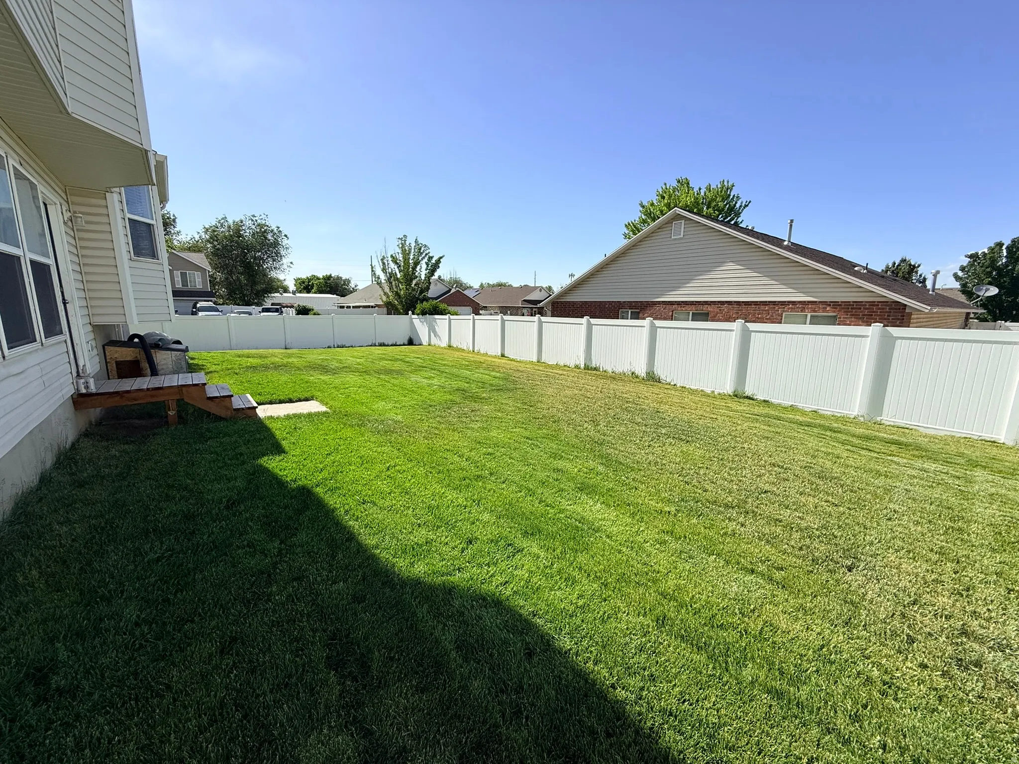 Expansive backyard featuring a lush lawn, complete white vinyl fencing, a partial wooden deck with steps, and a bay window on the home's exterior