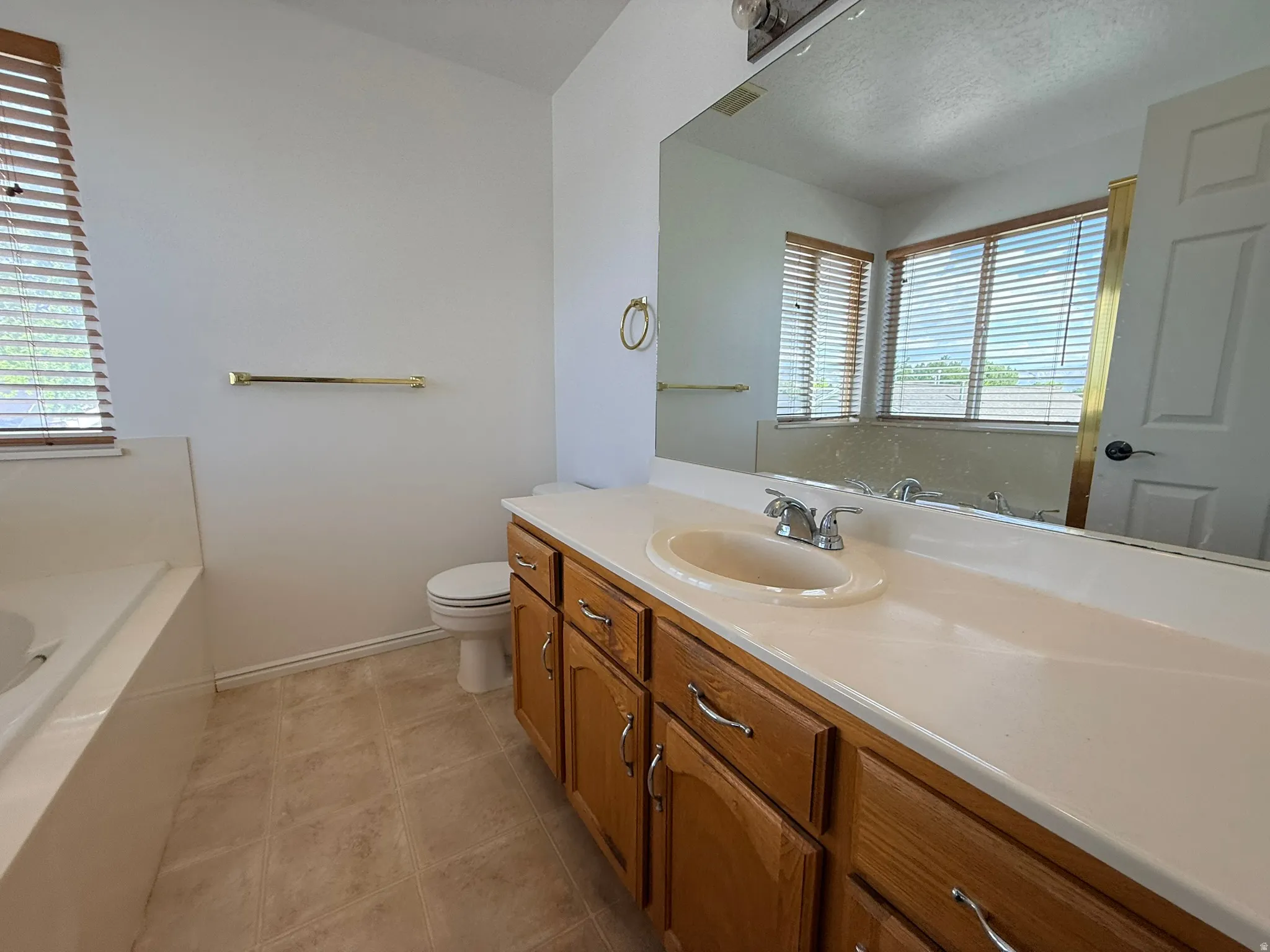 Bathroom featuring a built-in tub, wood-finish vanity with an integrated sink, and a large wall-mounted mirror