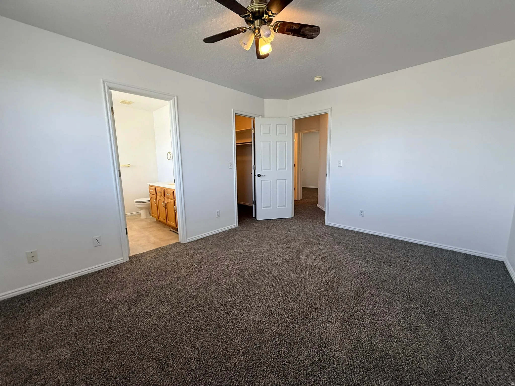 Carpeted room with white walls, a ceiling fan, and baseboard molding
