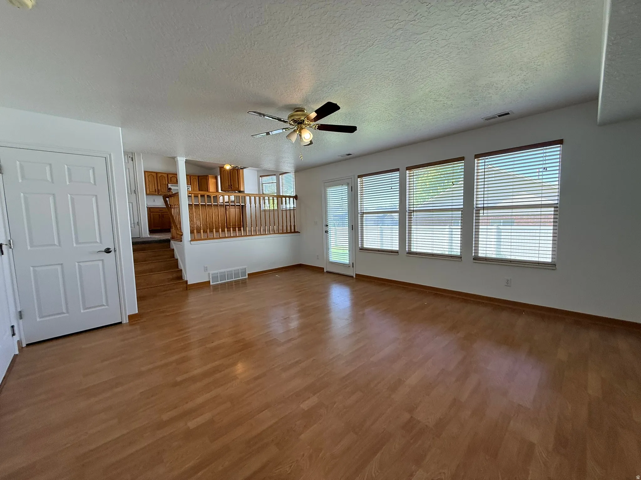 Spacious main living area featuring wood-finish flooring, a ceiling fan, and multiple windows with blinds