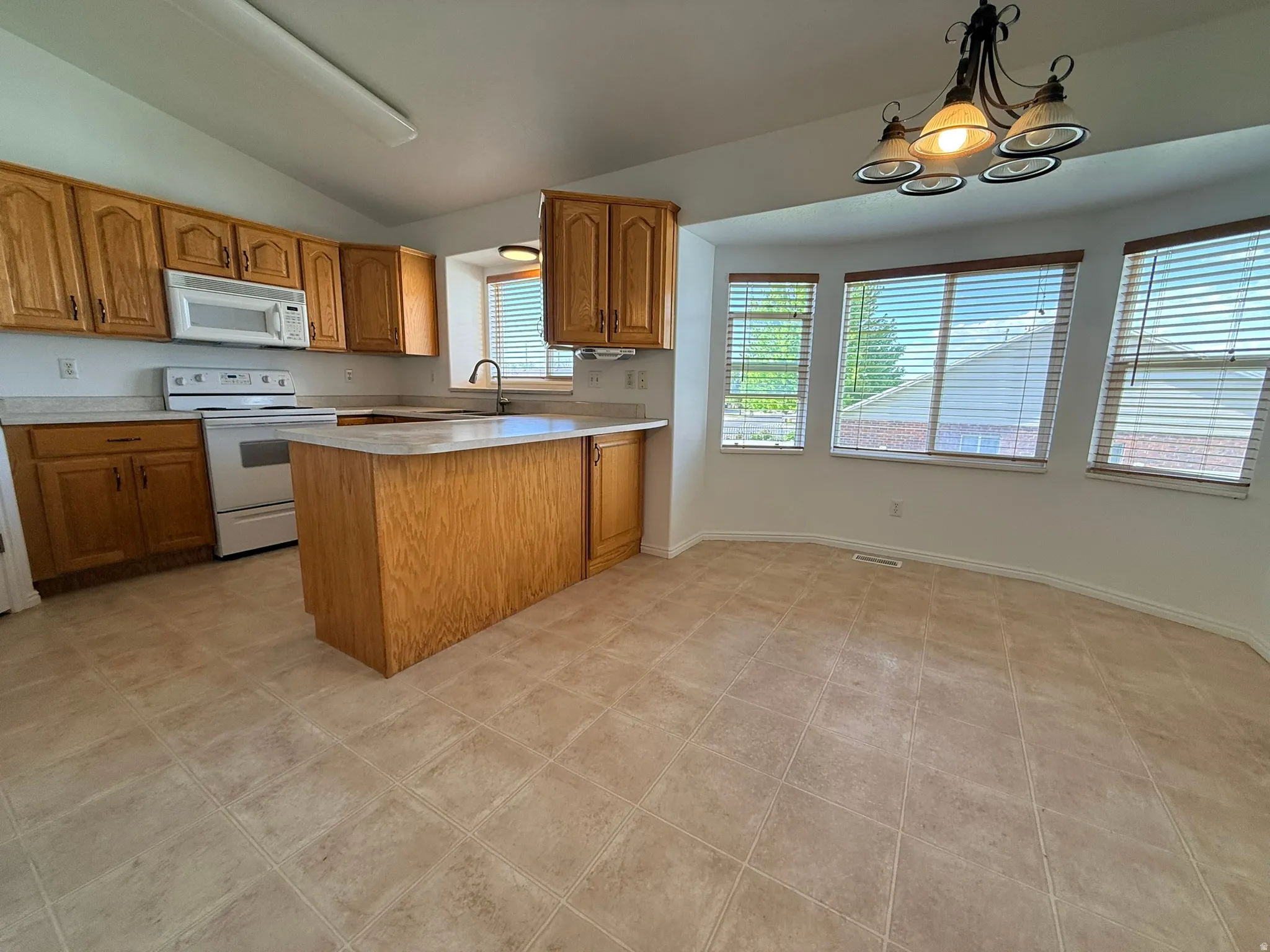 Kitchen area featuring wood cabinetry, white appliances, a center island with countertop seating, and tile flooring