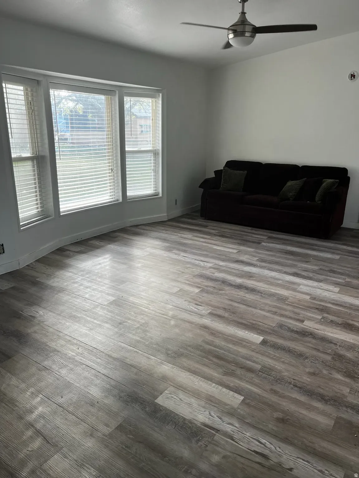 Spacious room featuring light wood-finish flooring, a bay window with blinds, and white walls
