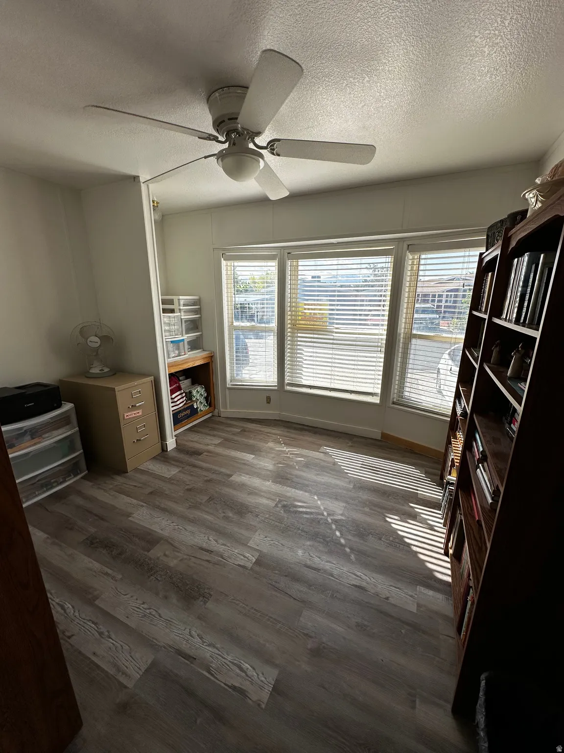 Room featuring wood-finish flooring, a ceiling fan with integrated lighting, and a bay window with horizontal blinds