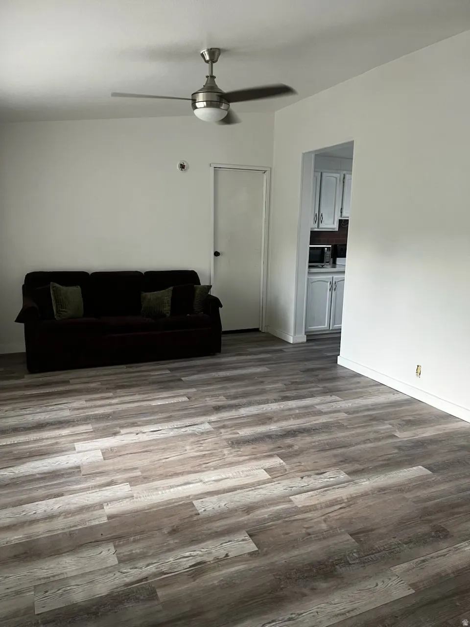Spacious room featuring wood-finish flooring, a ceiling fan with light fixture, and white wall finishes