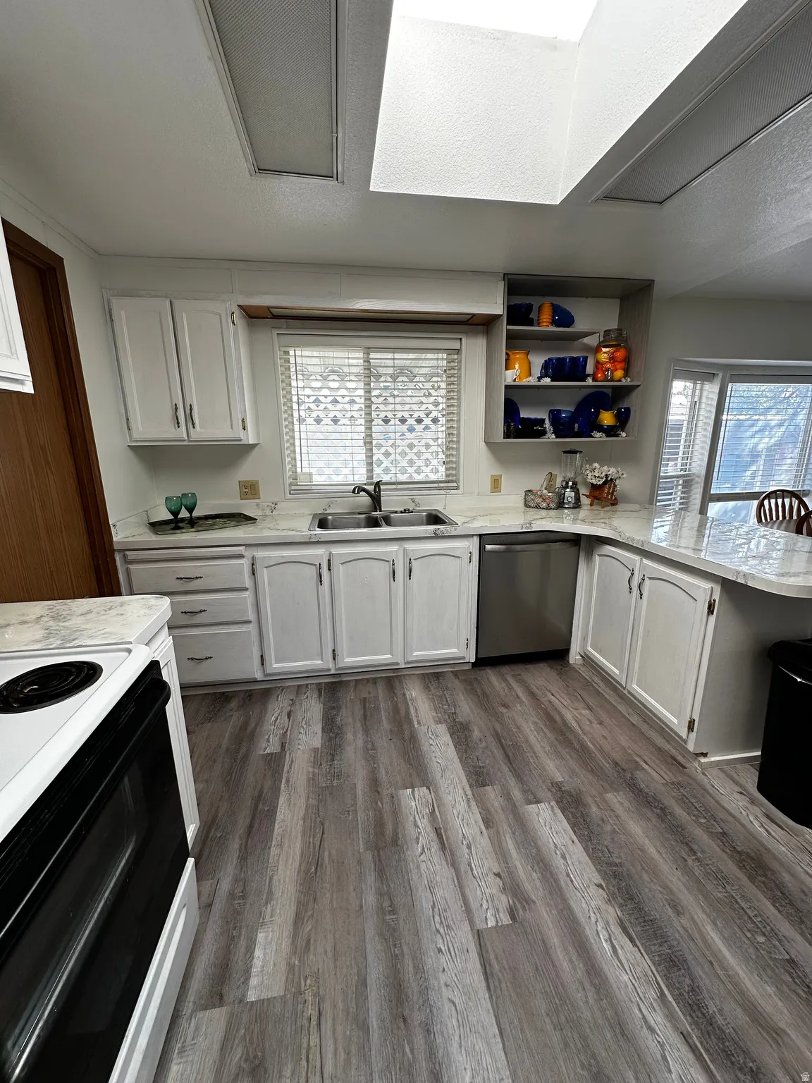 Kitchen featuring white cabinetry, light-toned countertops, a stainless steel dishwasher, a white range, and wood-finish flooring