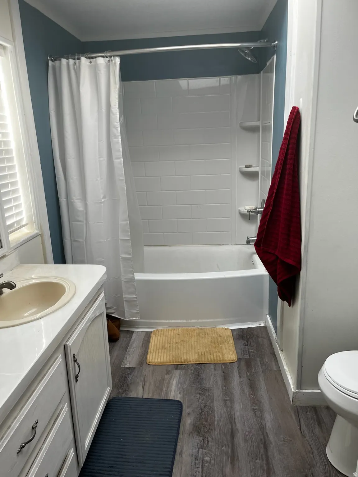 Bathroom featuring a white tub with subway tile surround, a single vanity with a laminate countertop, and wood-finish flooring