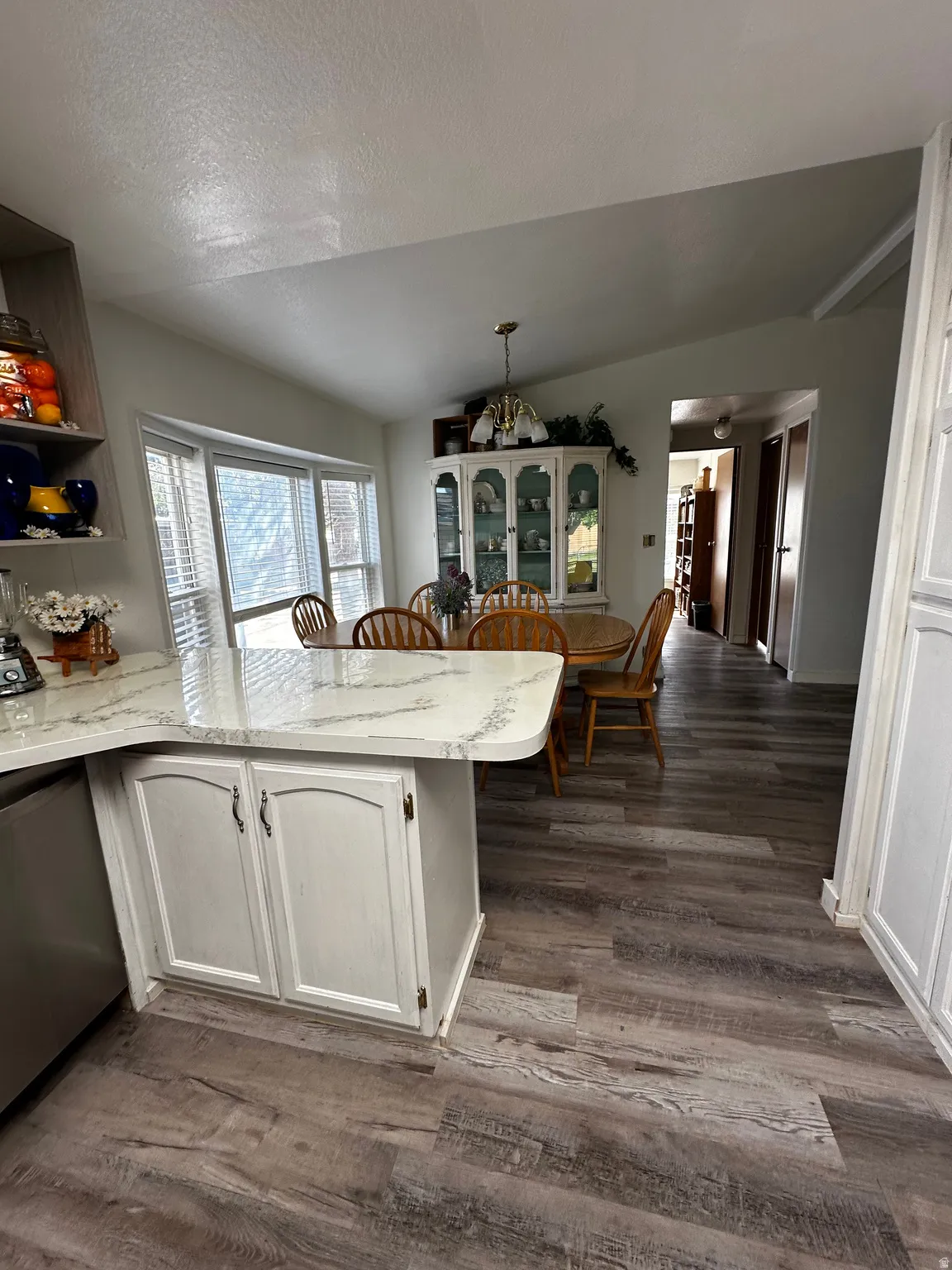 Kitchen-dining area featuring wood-finish flooring, a kitchen island with stone-look countertop, white cabinetry with silver-tone hardware, and a dining area with a chandelier