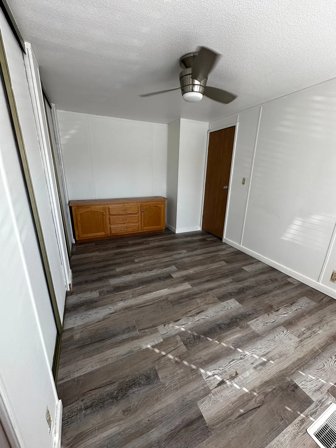 Spacious room featuring wood-finish flooring, white paneling, and a contemporary ceiling fan with integrated lighting