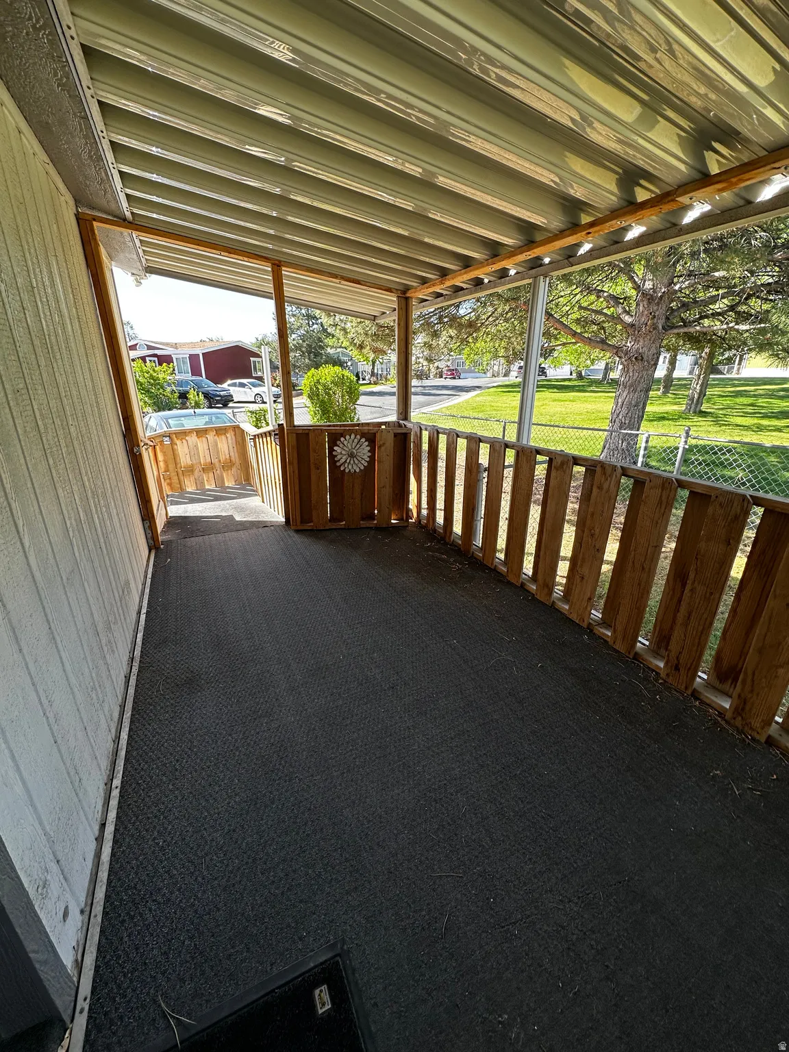 Covered porch featuring a corrugated metal roof, wood slat railing, and dark textured flooring