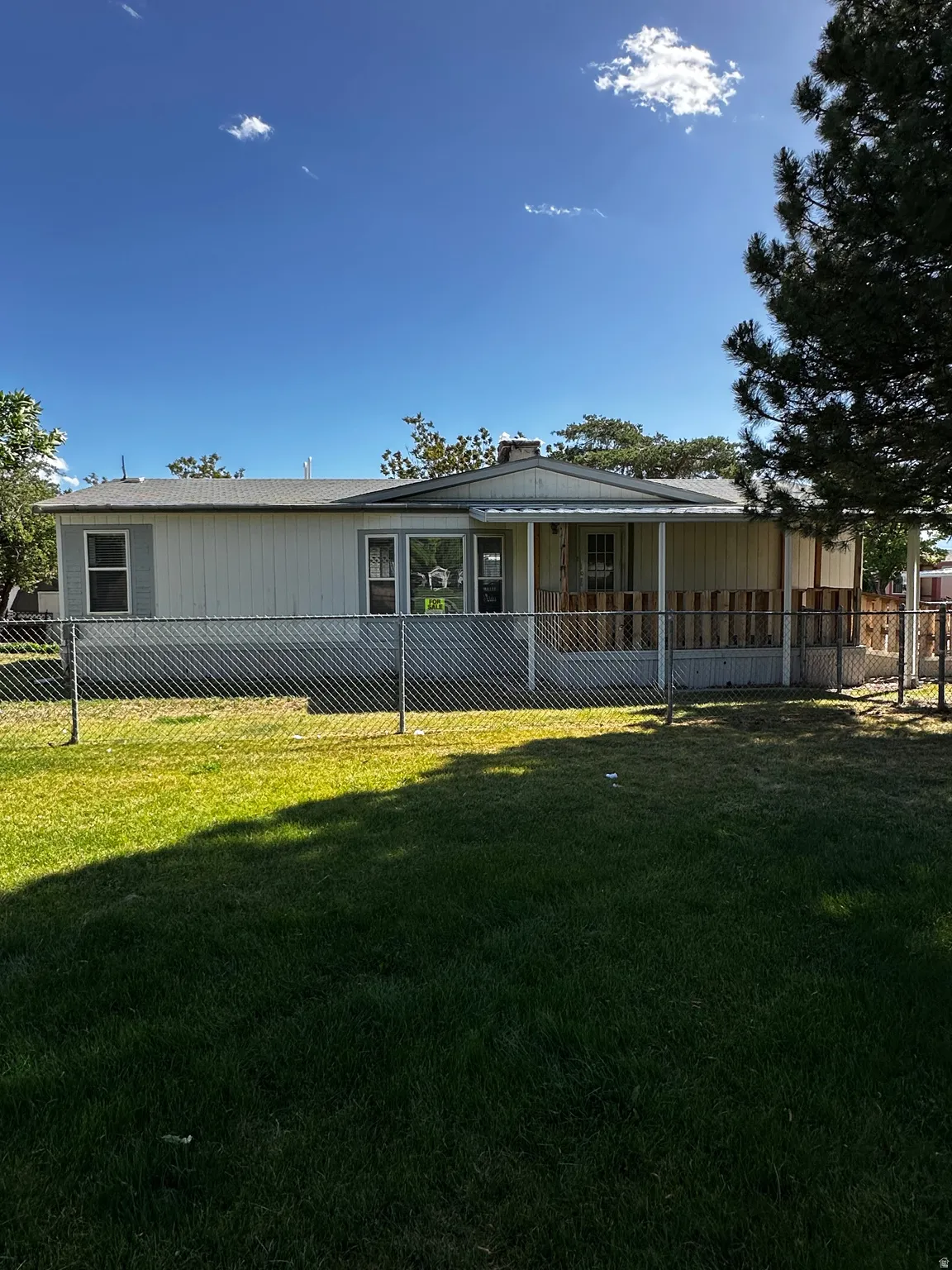 Single-story residence featuring light-colored siding, a covered front porch with white railing, and a chain-link fence enclosing a front lawn