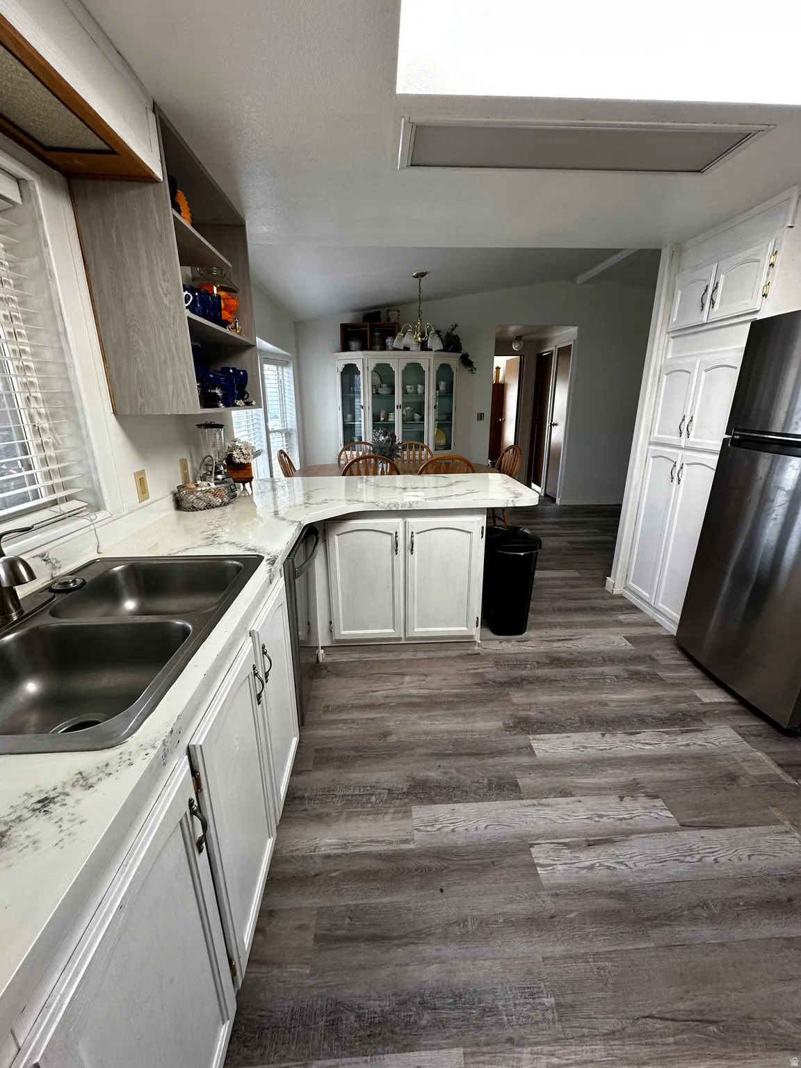 Kitchen featuring wood-finish flooring, white cabinetry, a double basin sink, light-toned countertops, and a skylight