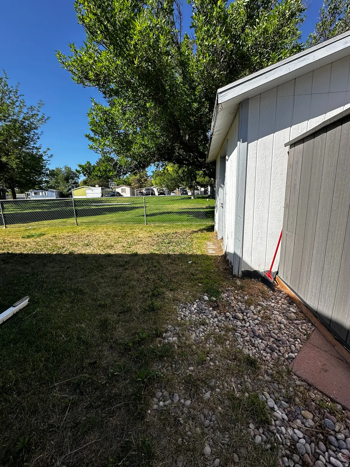White exterior siding with light gray trim, gravel landscaping, chain-link fencing, and mature trees